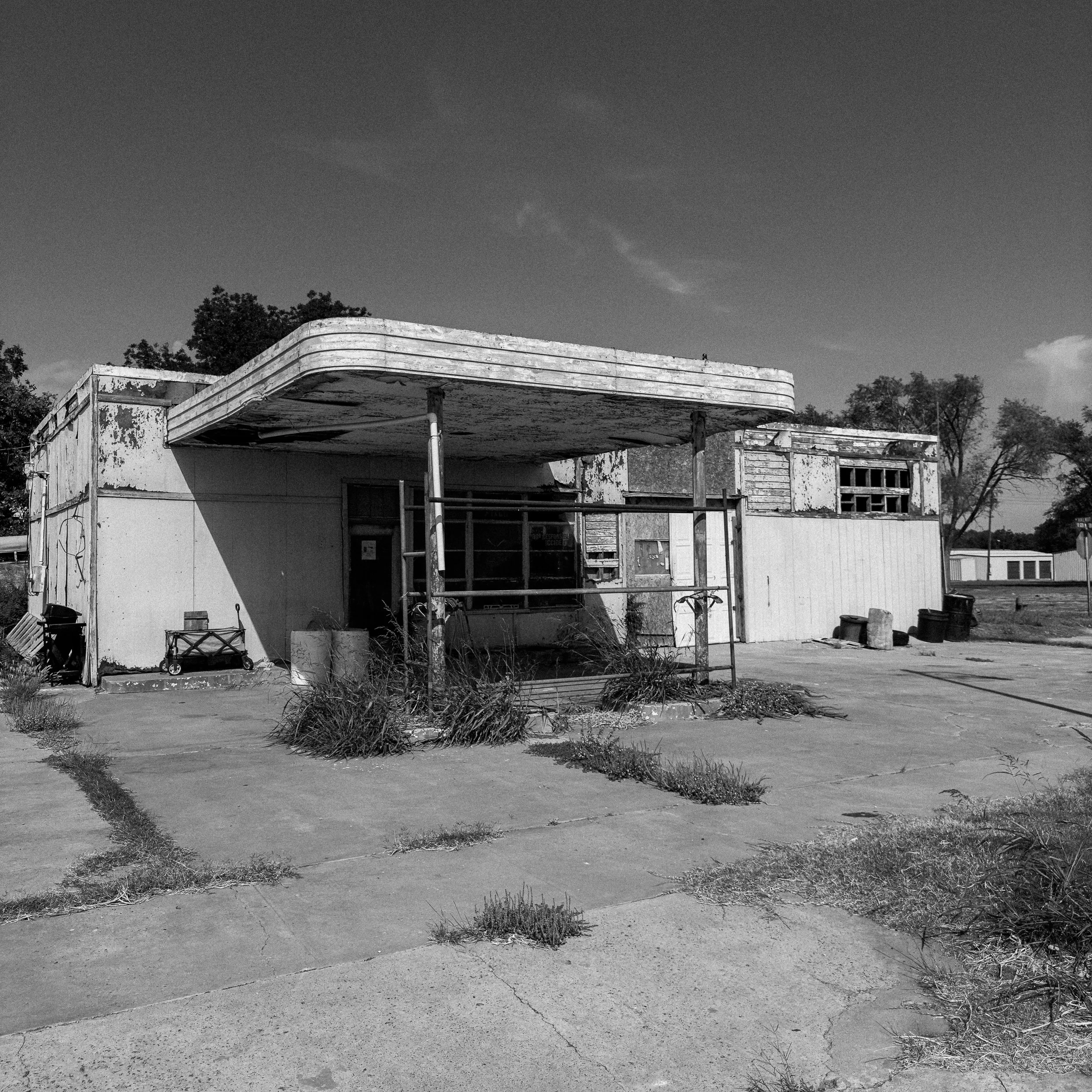 A derelict gas station with a sagging canopy, boarded windows, and scattered debris in the lot.