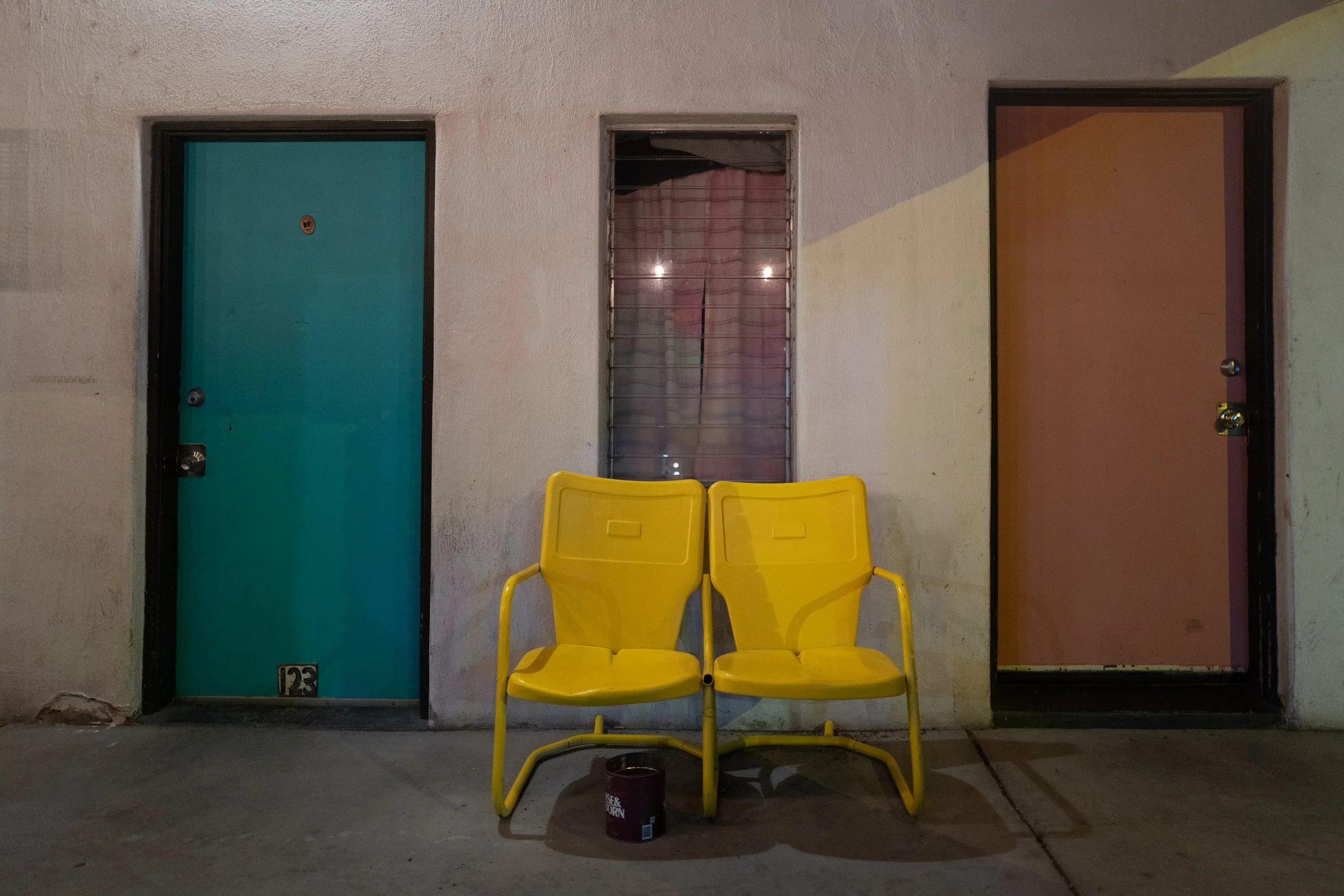 Two yellow metal chairs between colorful motel room doors at night.