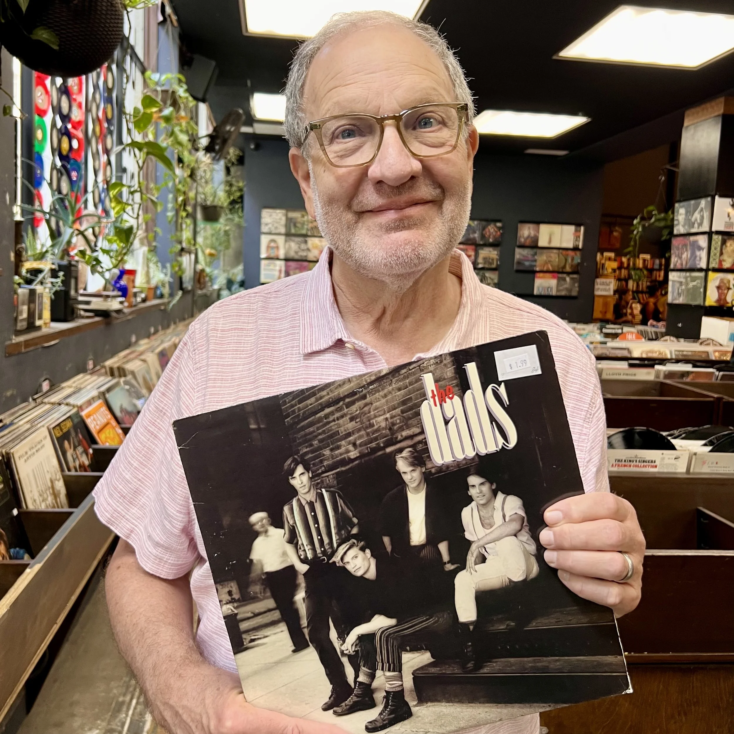 Richard Evnen smiling and holding a vinyl record album in a record store, surrounded by LP bins.