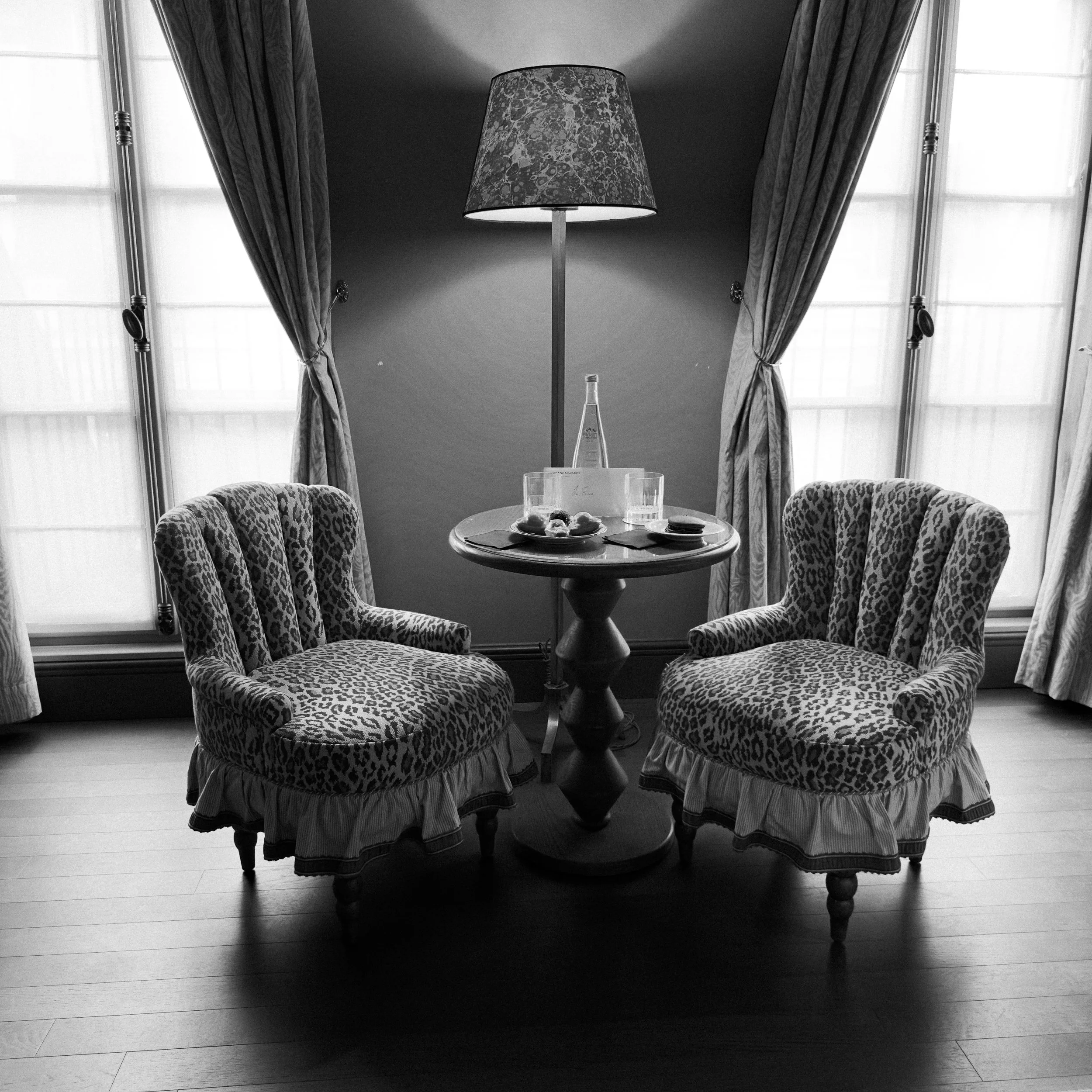 Two leopard-print upholstered chairs beside a glowing floor lamp between tall curtained windows.