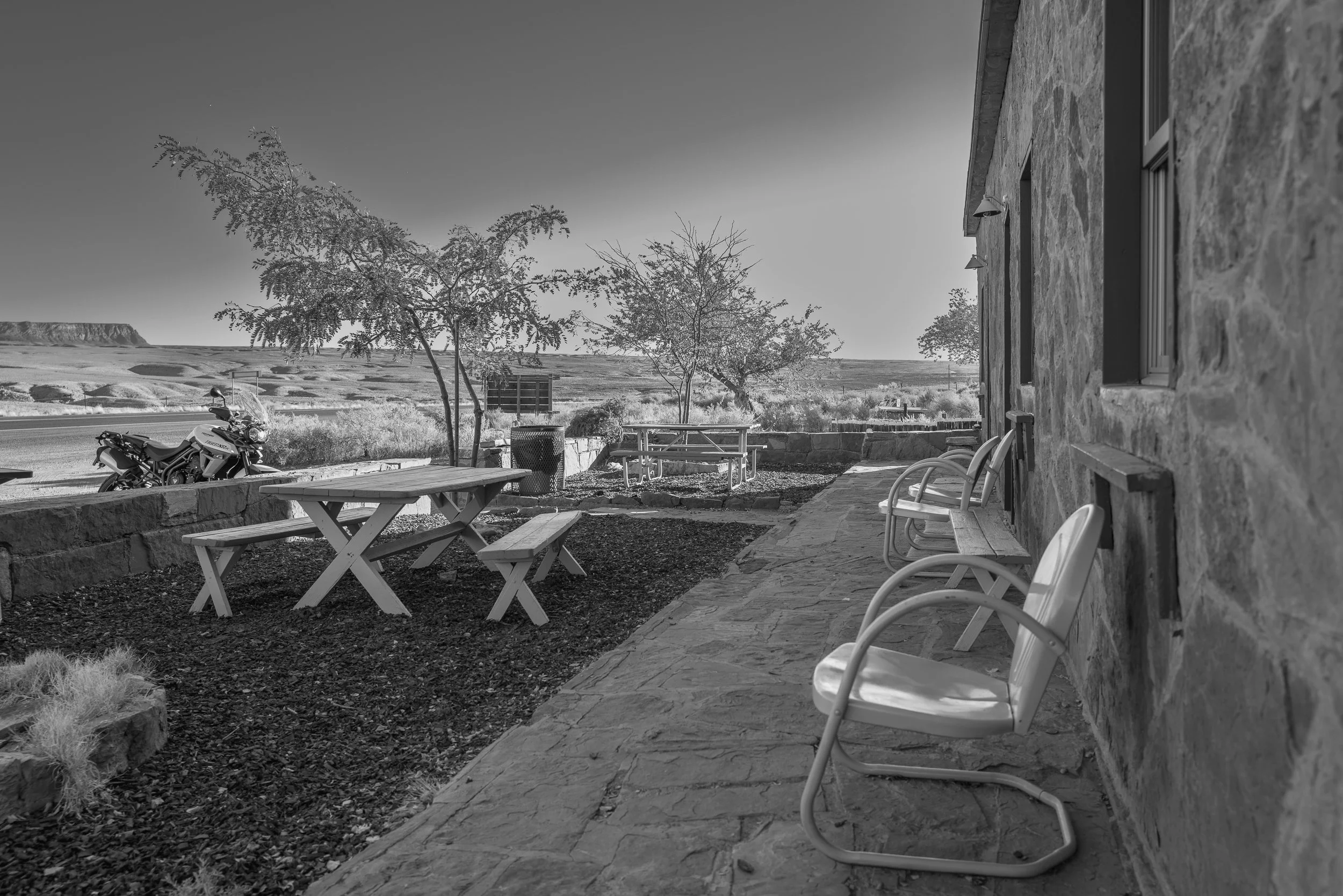 Metal patio chairs on a stone walkway beside a picnic table, with desert mesas in the distance.