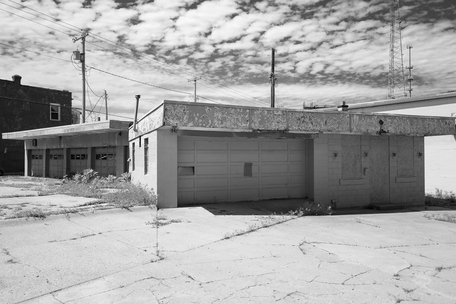 A closed cinderblock service station with a garage bay under a cloud-streaked sky.