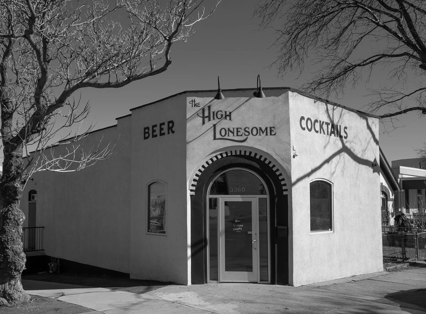 A rounded corner building with The High Lonesome beer and cocktails signage beneath bare tree branches.