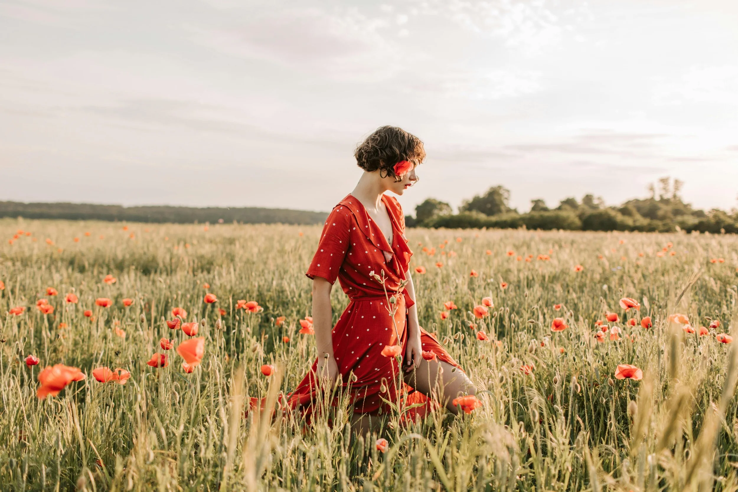 Woman in a red dress standing in a poppy field, looking down pensively, representing reflection and self-discovery often experienced by late-diagnosed autistic women.