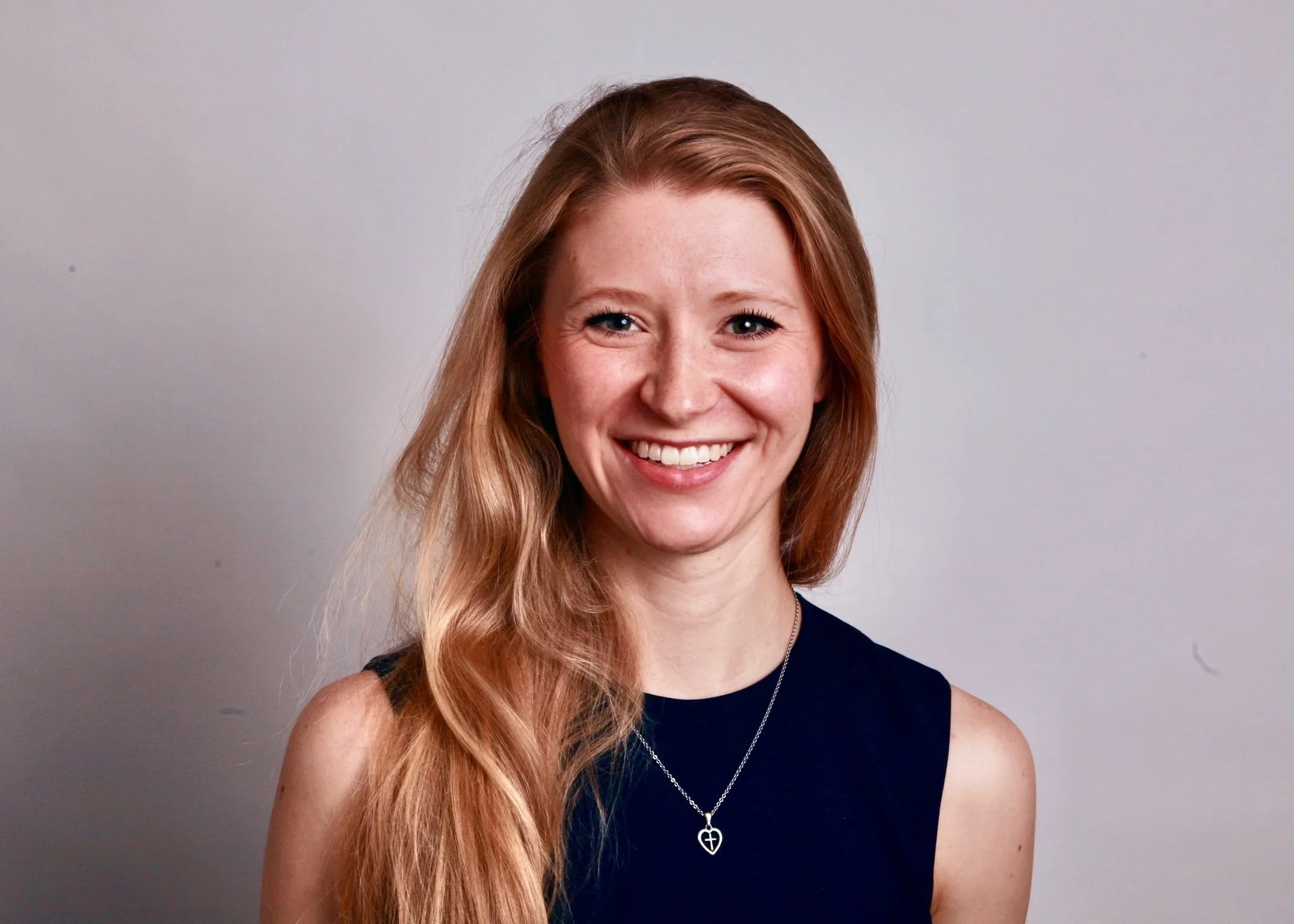 Gentry Higgins smiling wearing a black sleeveless top and a delicate necklace.