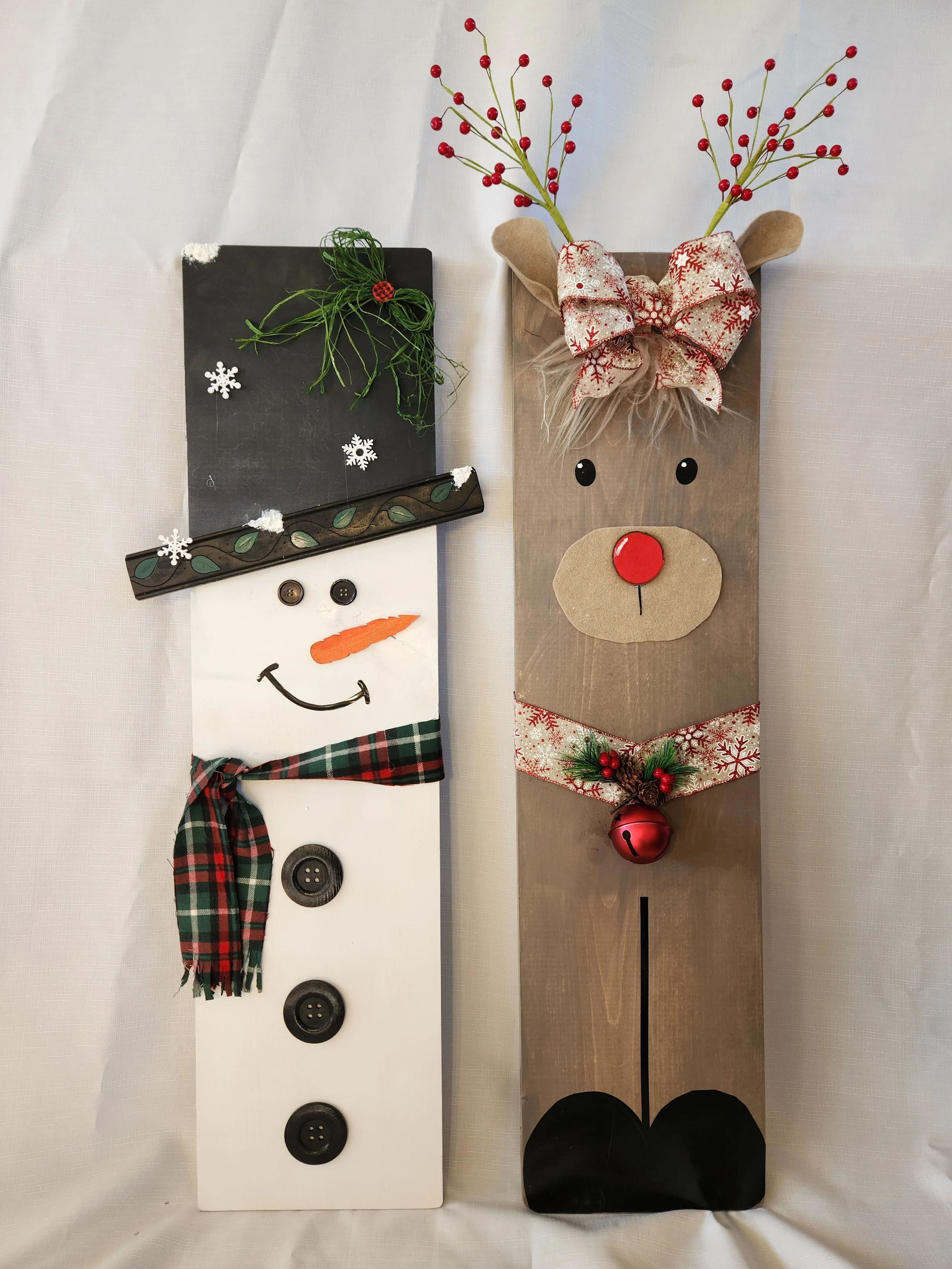 Three vertical wooden signs with the letter 'J' and 'Y' painted on them in white and red, decorated with holiday wreaths and greenery.