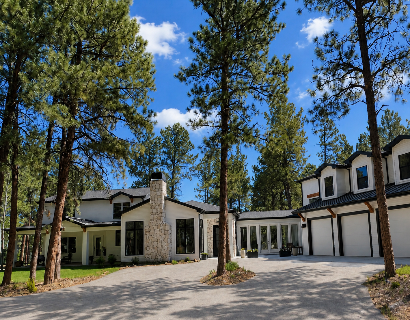 Large stone house with arched windows and a driveway with a landscaped circular flower bed featuring a small tree and colorful flowers.