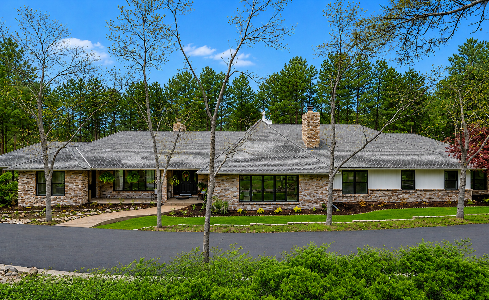 A modern house with a dark gray exterior, stone accents, and a large deck surrounded by trees, with an American flag on a flagpole in front.