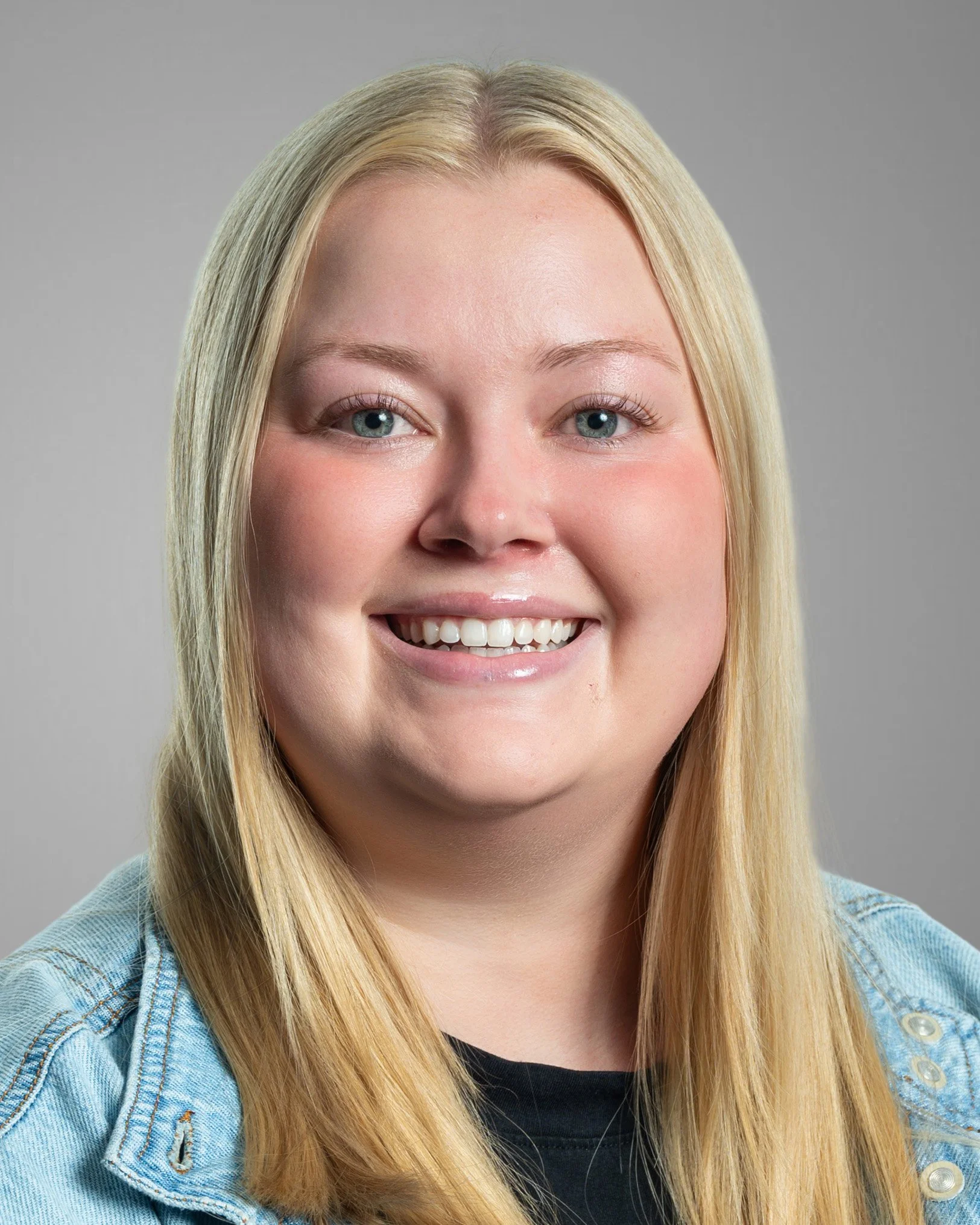 Portrait of a smiling person with long blonde hair in a black shirt against a white background.