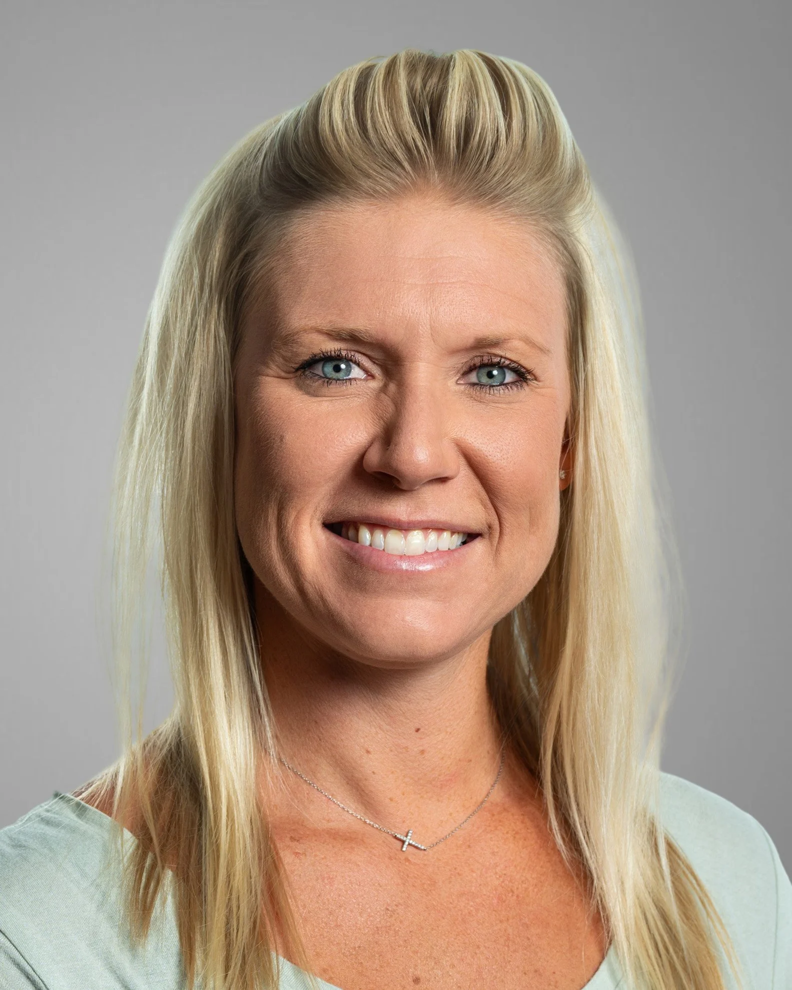 Smiling woman with long blonde hair wearing a blue top with ruffled sleeves, white background.