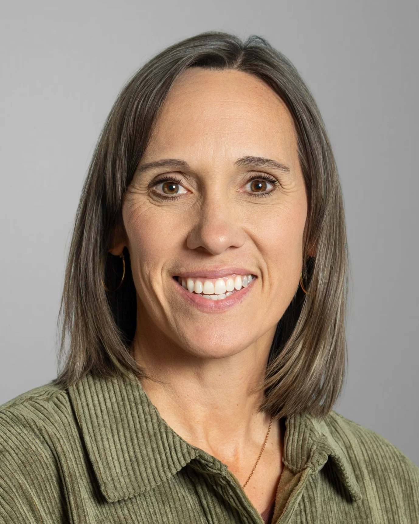 Smiling woman wearing a tan coat with short brown hair