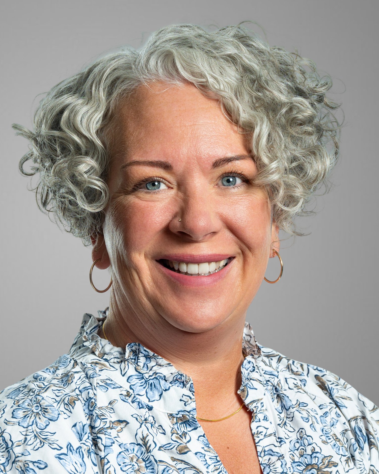 Person with short curly hair wearing a denim jacket and smiling.