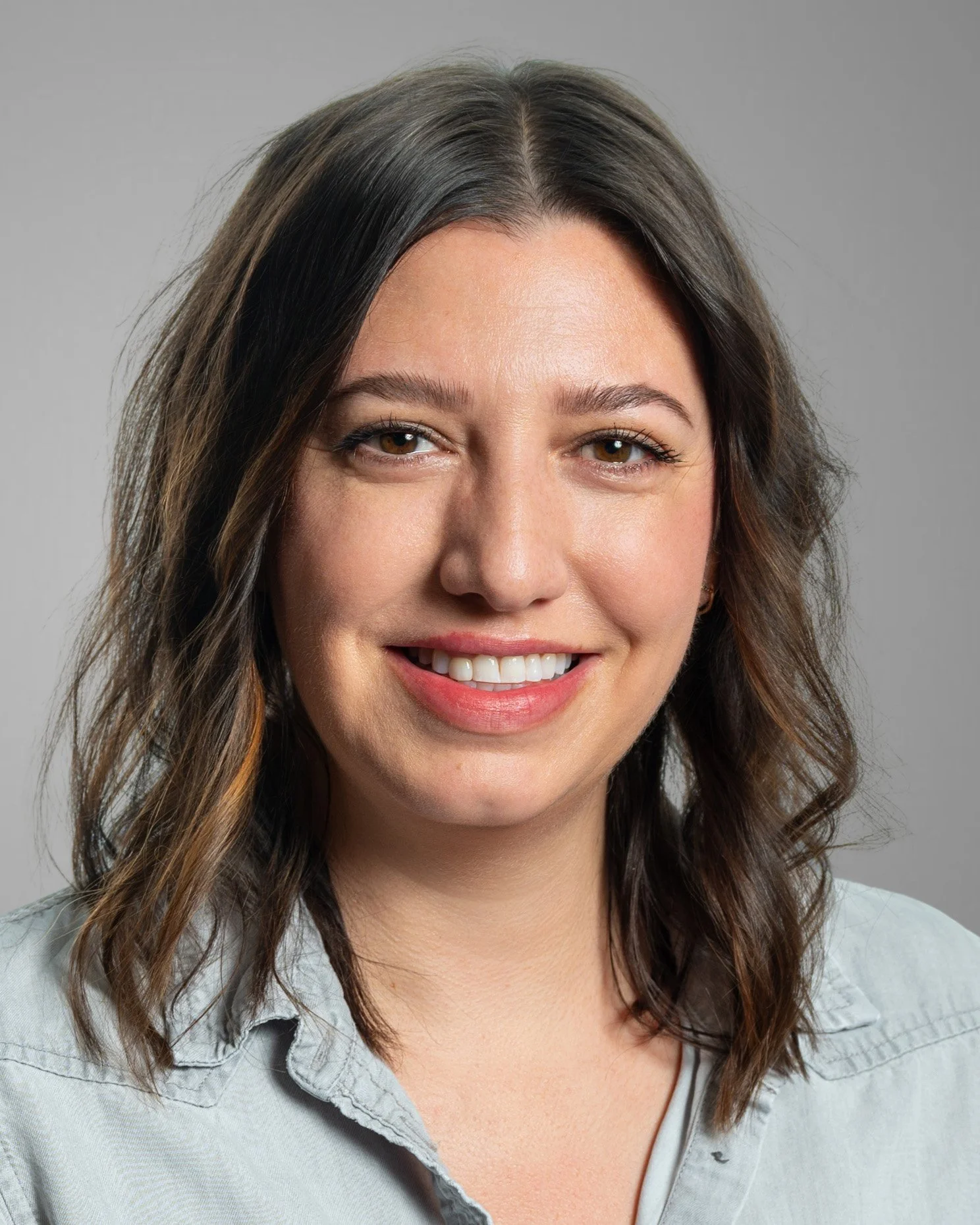 Smiling person with long brown hair wearing a light blue shirt.