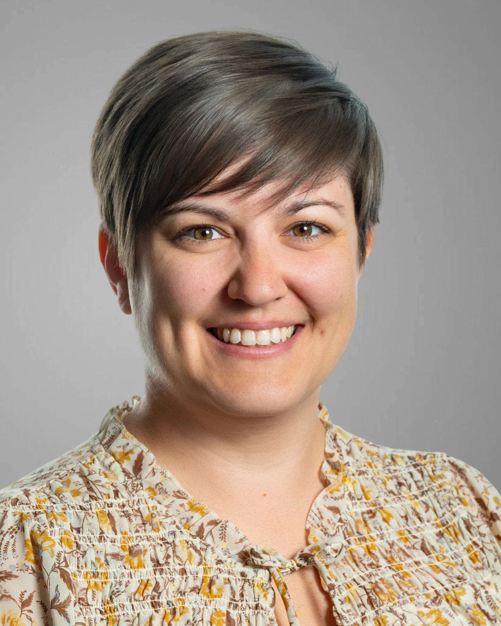 Smiling person with short brown hair wearing a green floral top.