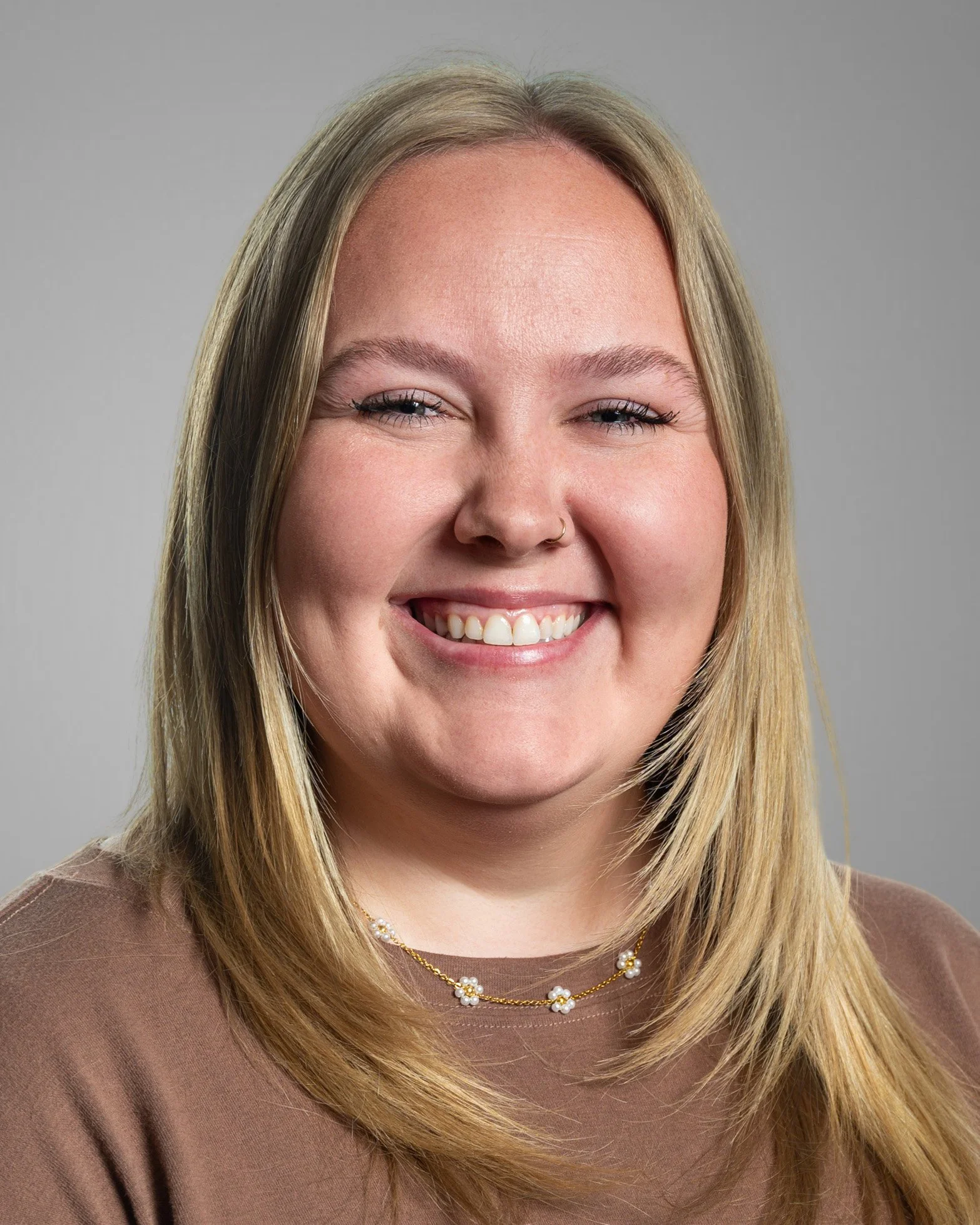 Smiling woman with long blonde hair, wearing a black top and white shirt, against a white background.