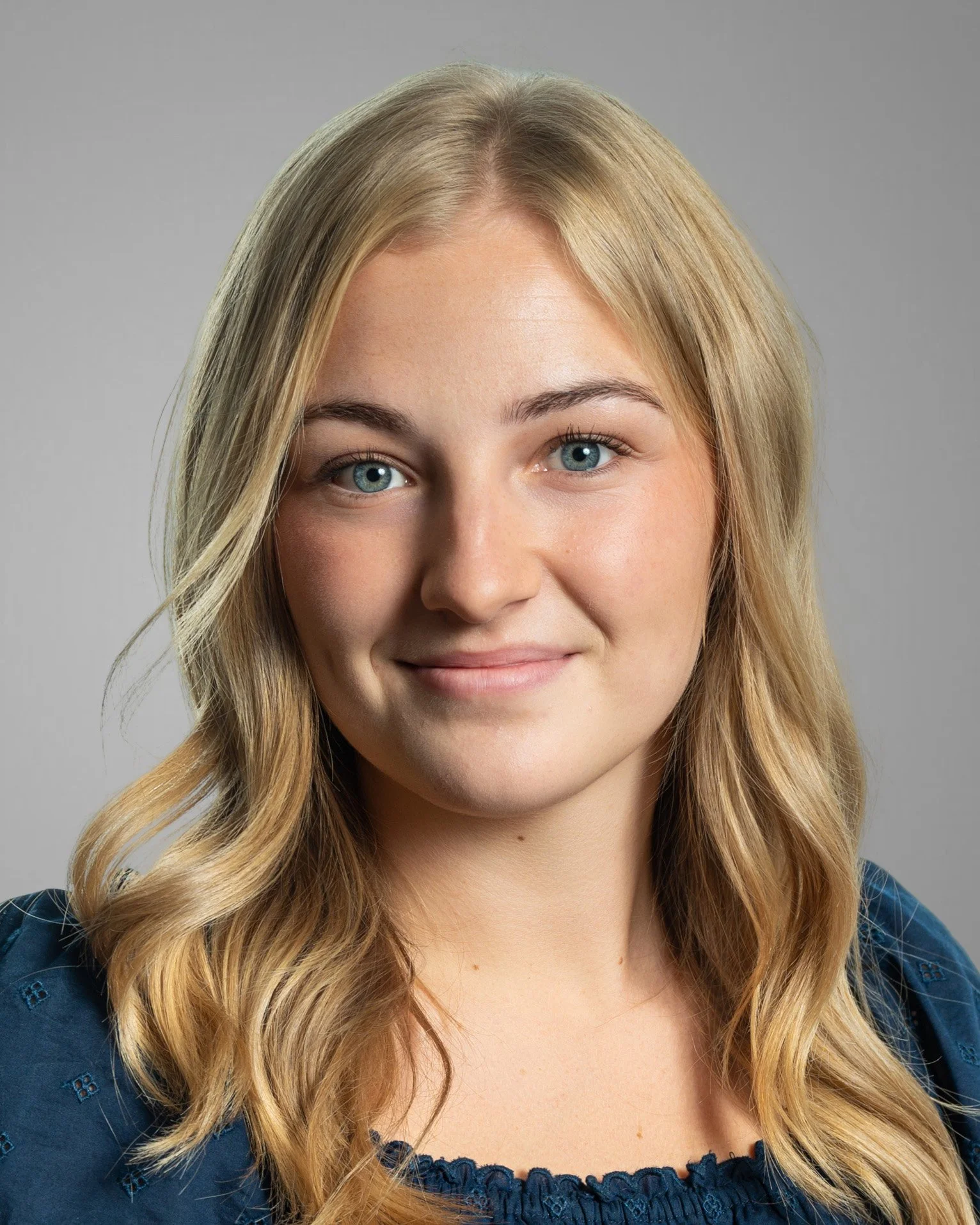 Smiling person with long hair and black top against white background