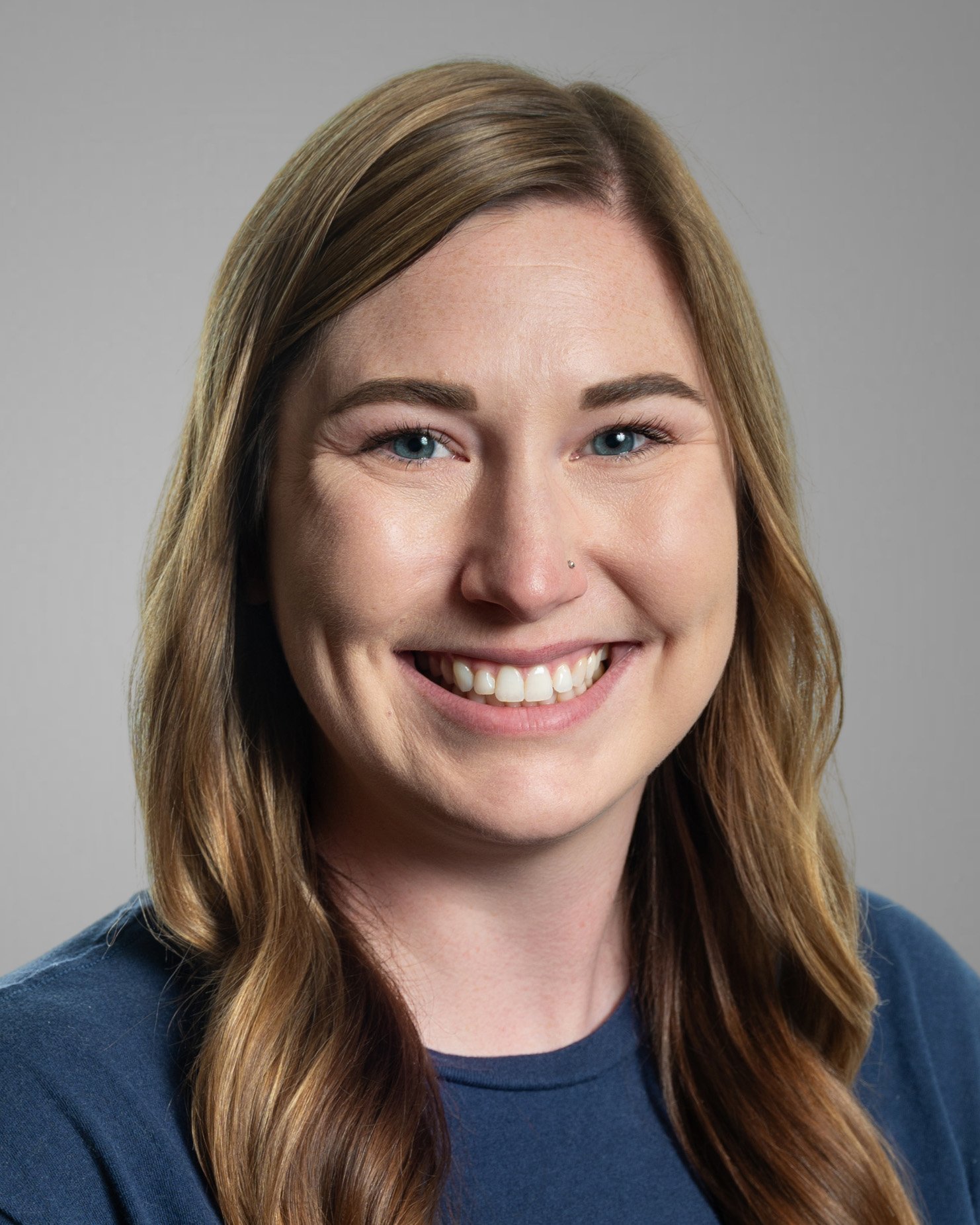 Smiling woman with long brown hair in a blue floral shirt against a white background.