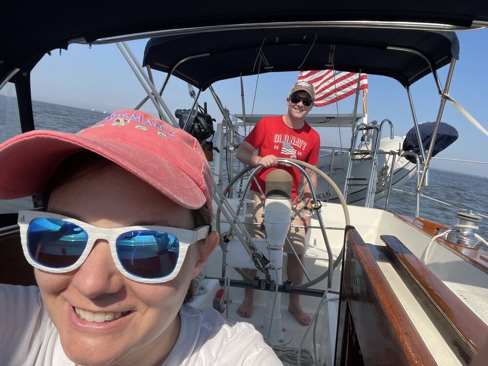 Kirsten taking a selfie with Brian driving Samba, our Morgan 382 sailboat, on a sunny day on the Chesapeake Bay.