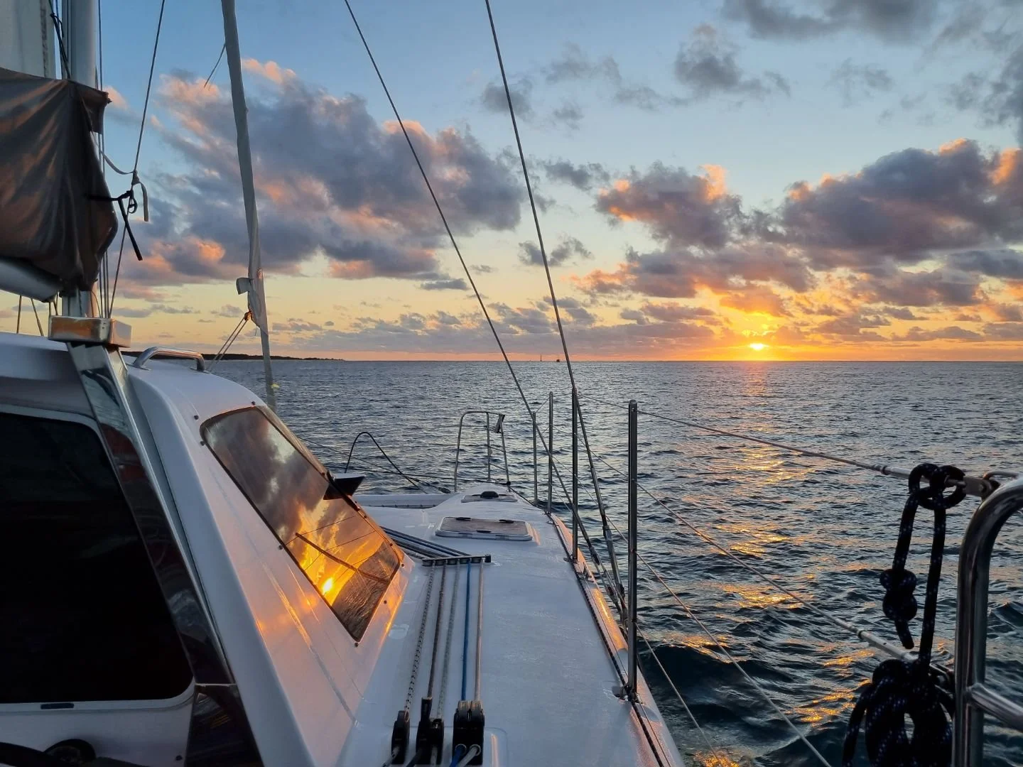 View of a sailboat on the ocean during sunset with clouds in the sky, reflected in the boat's window.