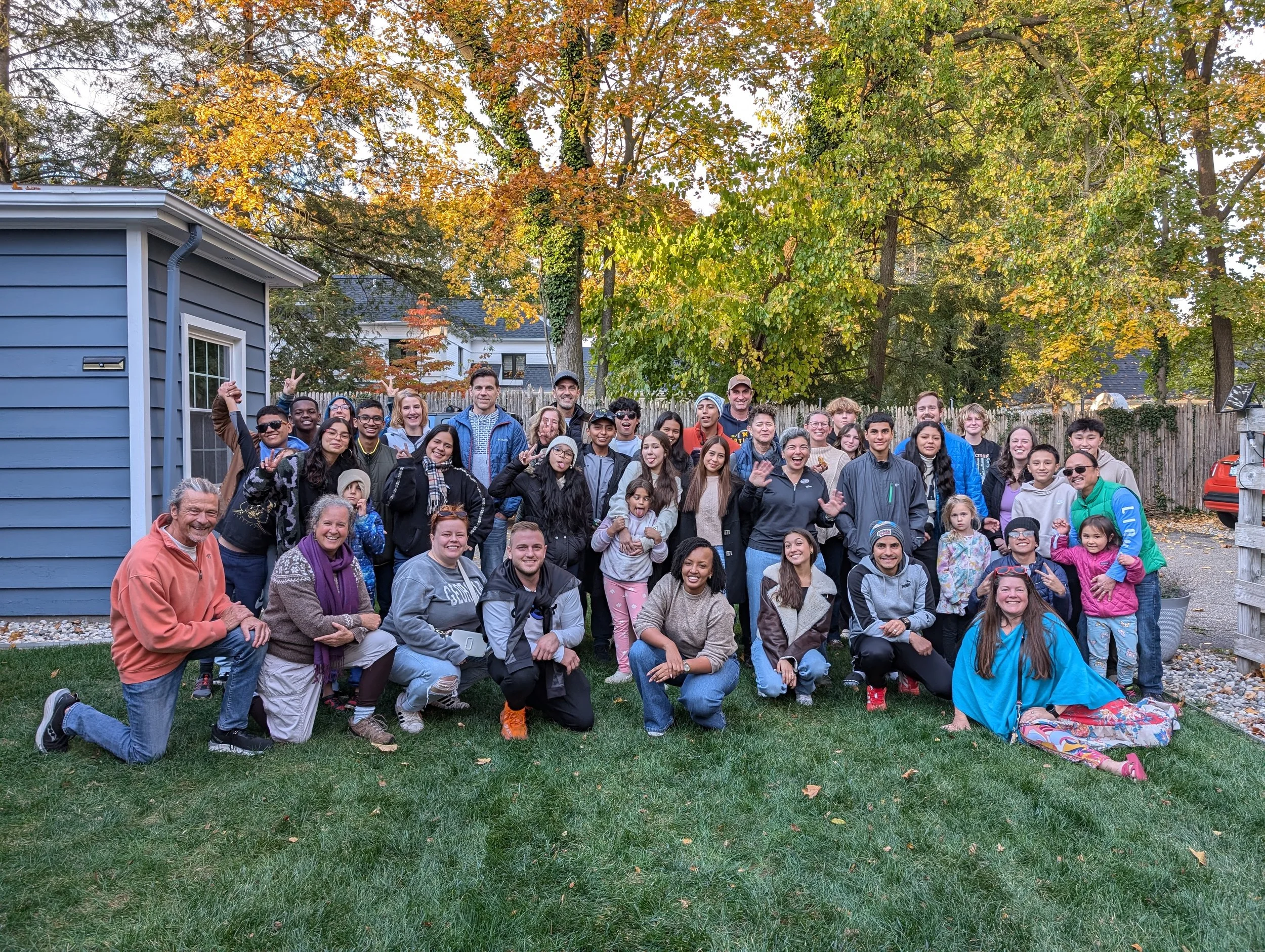 A large group of people is pictured with LAYA participants in a backyard in the fall at a Global Ties Kalamazoo gathering.