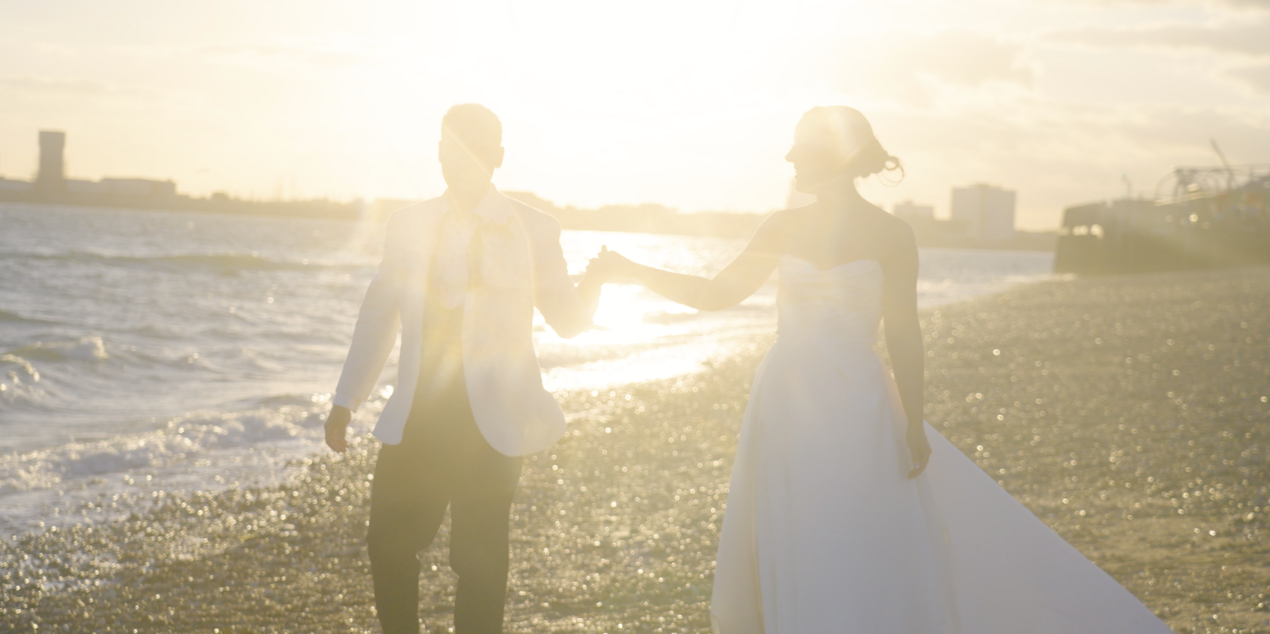 A couple in wedding attire holding hands on a beach at sunset.