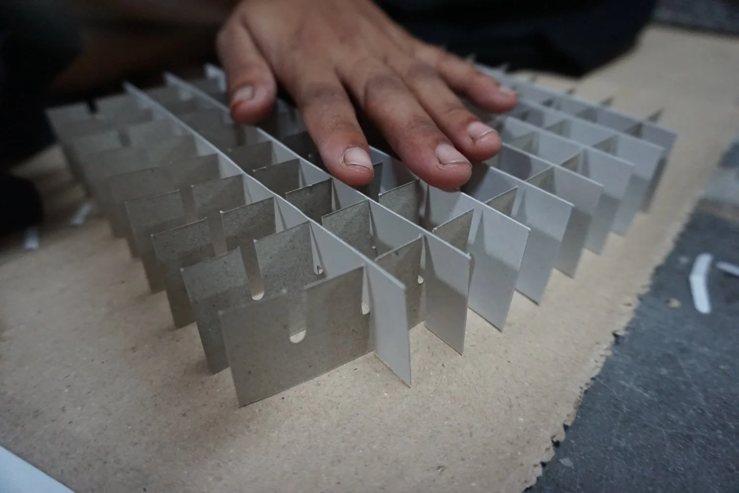 Close-up of a hand touching a metal grid or frame with multiple rectangular compartments, on a work surface.