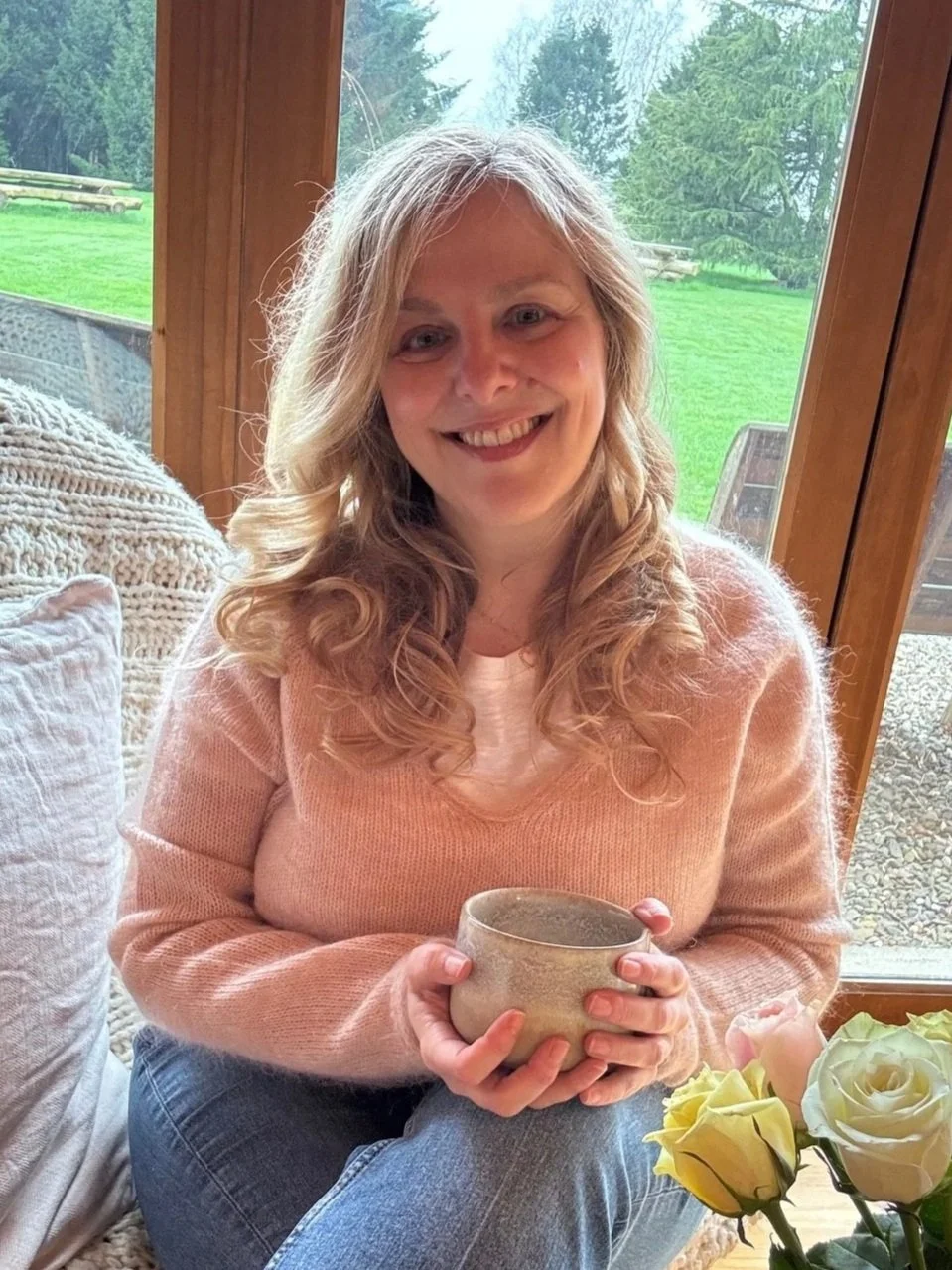 Sarah Pritchard, Master Somatic Movement Therapist, smiling warmly and holding a tea bowl in her light-filled Shrewsbury clinic, offering a welcoming space for somatic therapy and movement enquiries