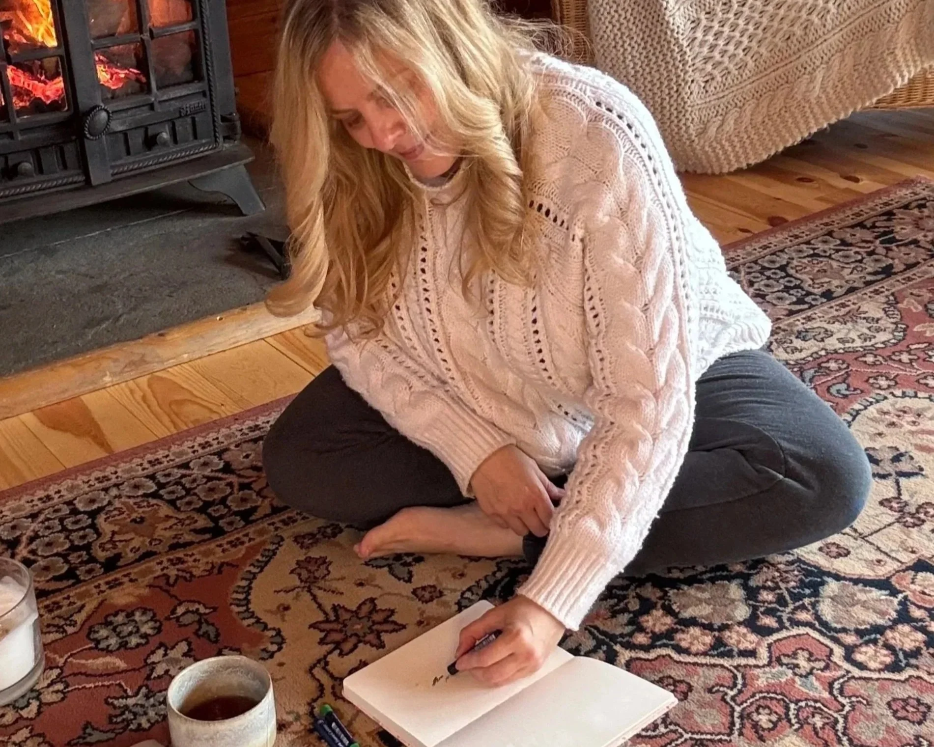 Sarah Pritchard, a Master Somatic Movement Therapist, engaging in the SomaSoul expressive arts process using drawing and movement by a warm fire in her Shrewsbury cabin..