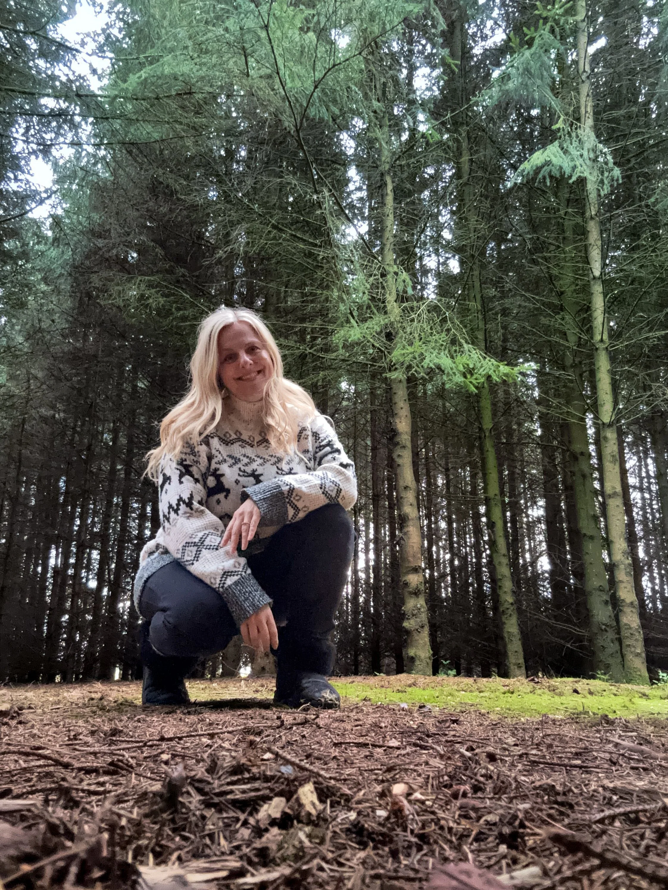 Sarah Pritchard MSMT MSME squatting grounded among the pine trees in the private woodland grounds at Newton Meadows in Shropshire.