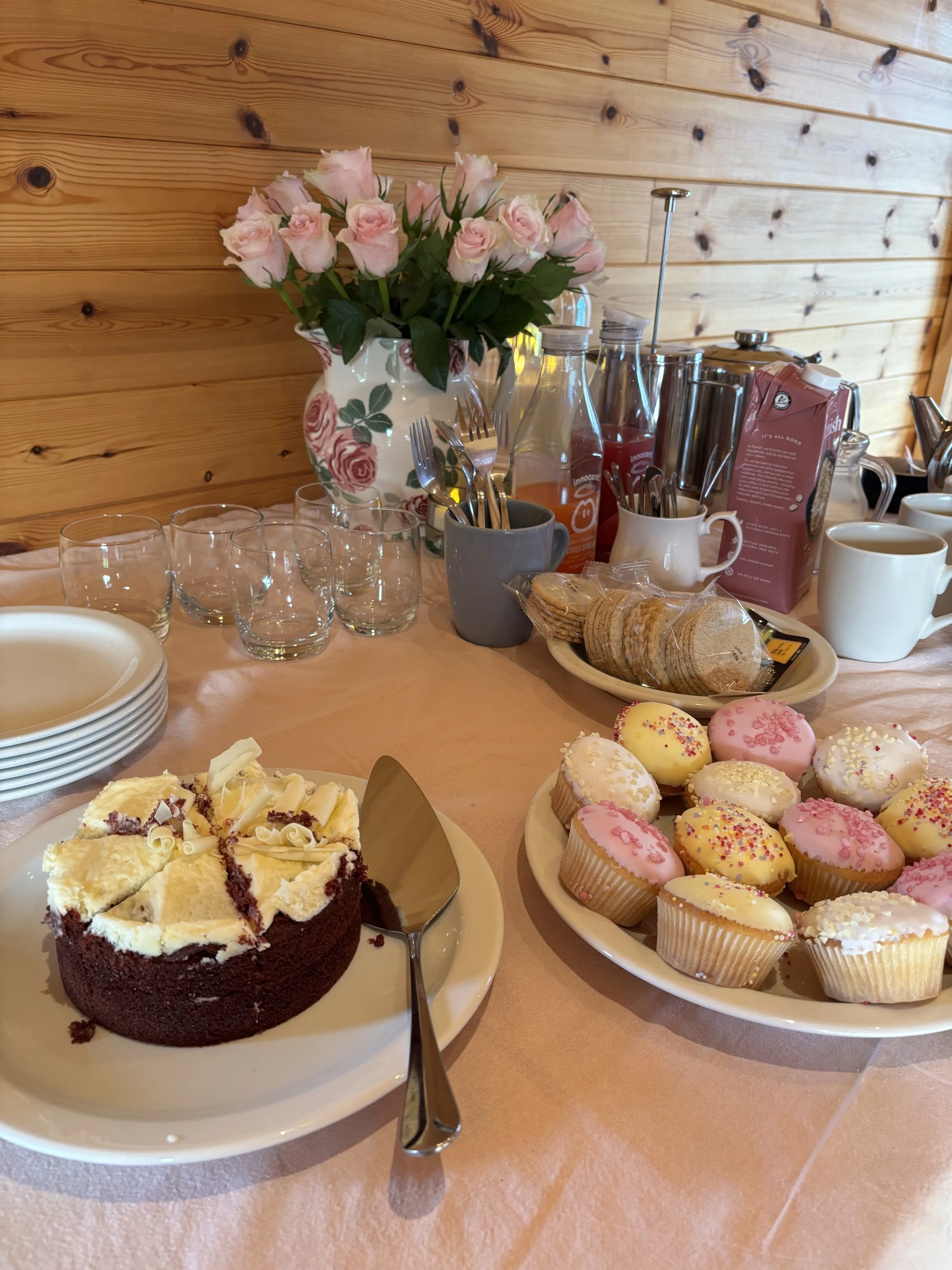 Delicious retreat refreshments including red velvet cake, iced cupcakes, hot drinks, and fresh pink roses at Newton Meadows in Shropshire.
