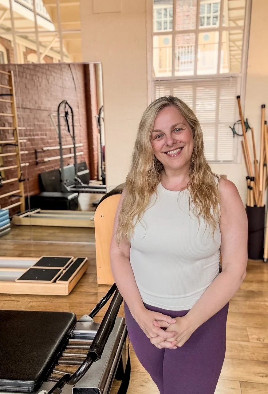 Sarah Pritchard, ISMETA Master Somatic Movement Therapist & Educator (MSMT/MSME) and 3rd Generation Pilates Specialist. In the Jewellery Quarter Pilates studio, surrounded by classical Pilates equipment, mirrors, and training apparatus.