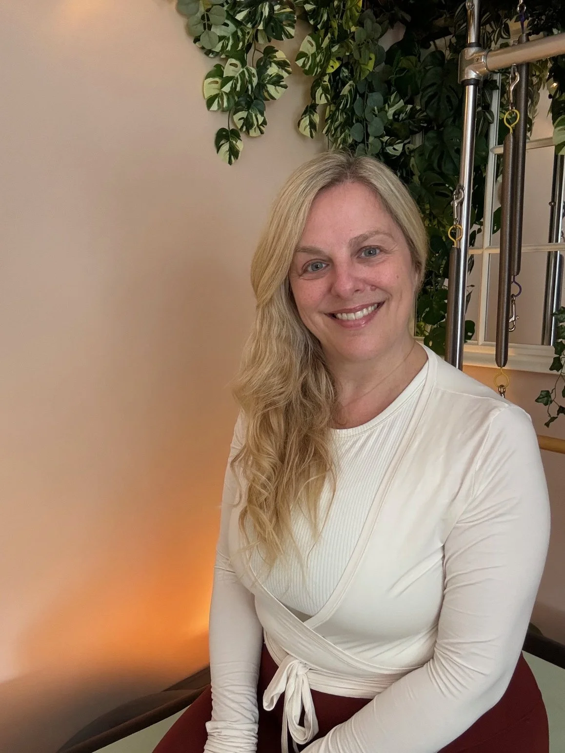 Sarah Pritchard, certified Pre and Post Natal Pilates Specialist, smiling next to her Pilates reformer machine in her virtual studio.