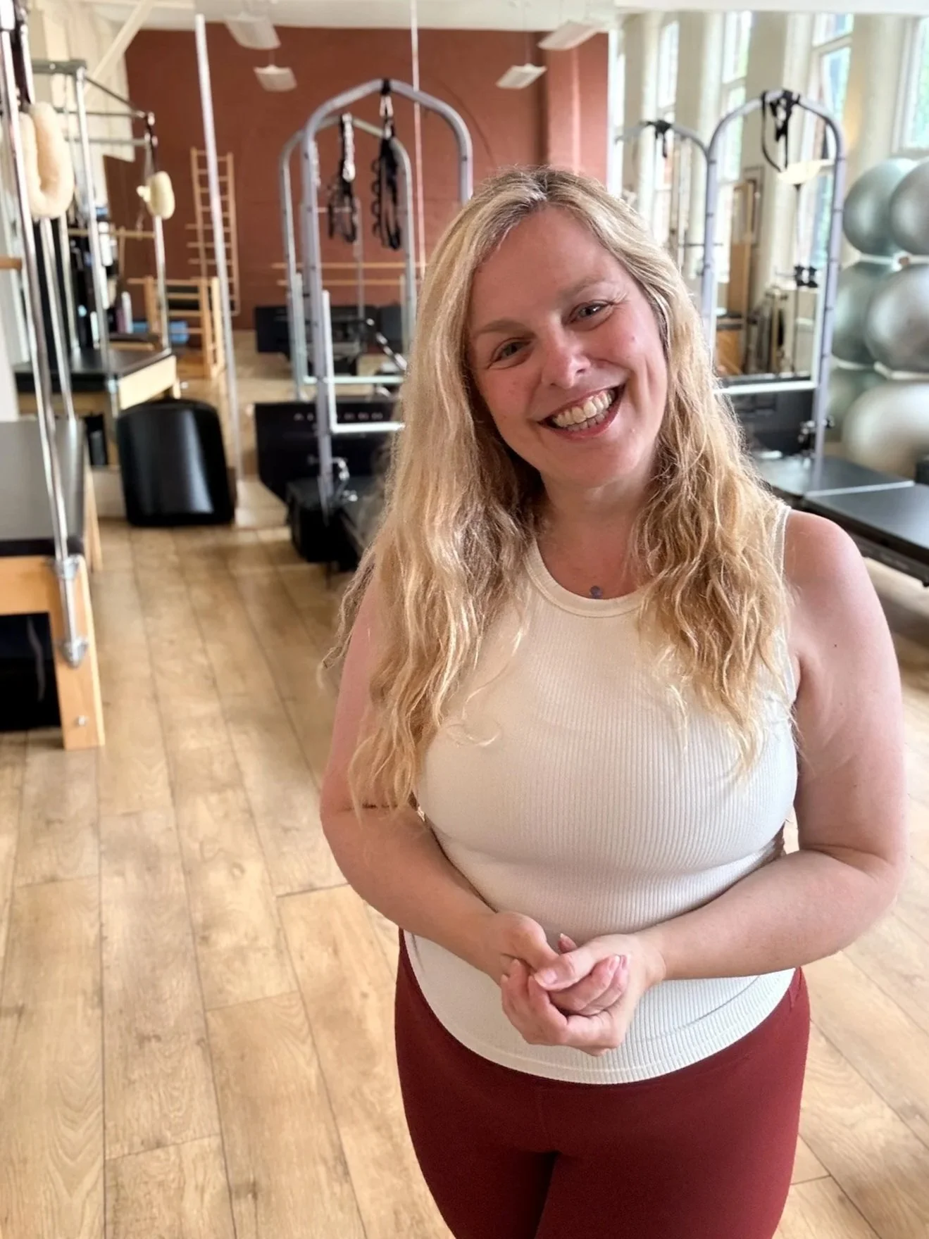 Image of Sarah Pritchard in the Cool Pilates studio Jewellery Quarter Birmingham smiling with tall windows and specialized Pilates apparatus