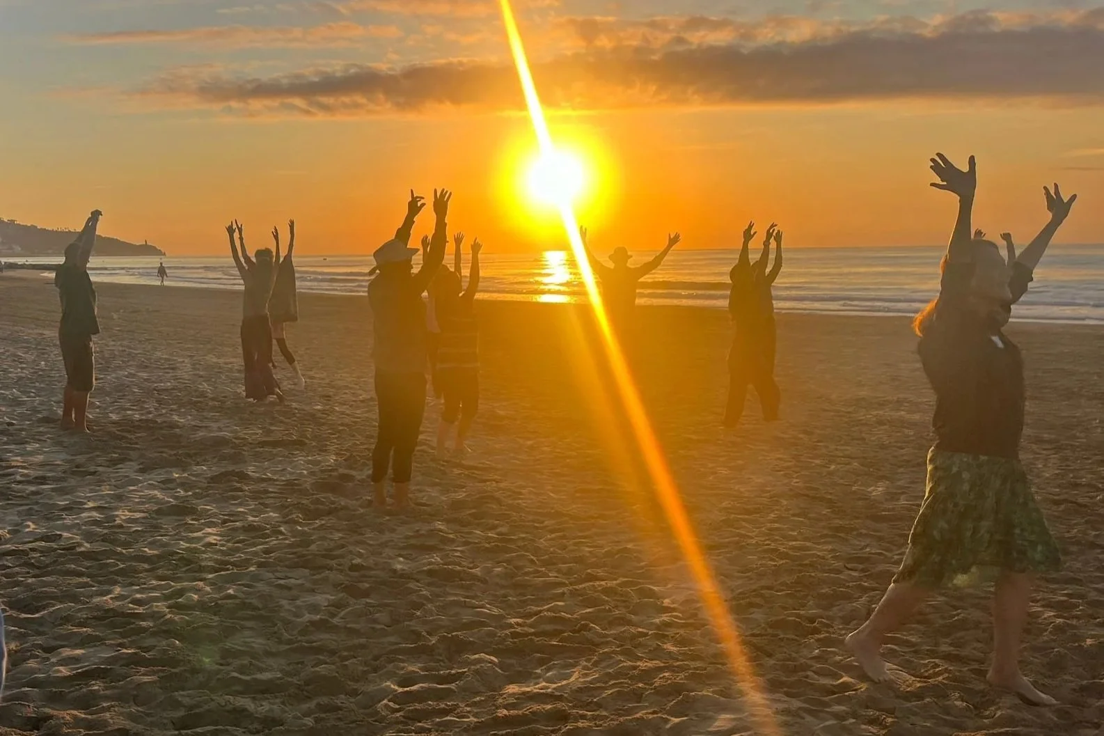 Somatic Therapist Sarah Pritchard practicing a collective embodiment sequence with international colleagues on the beach in Spain during the ISMETA conference