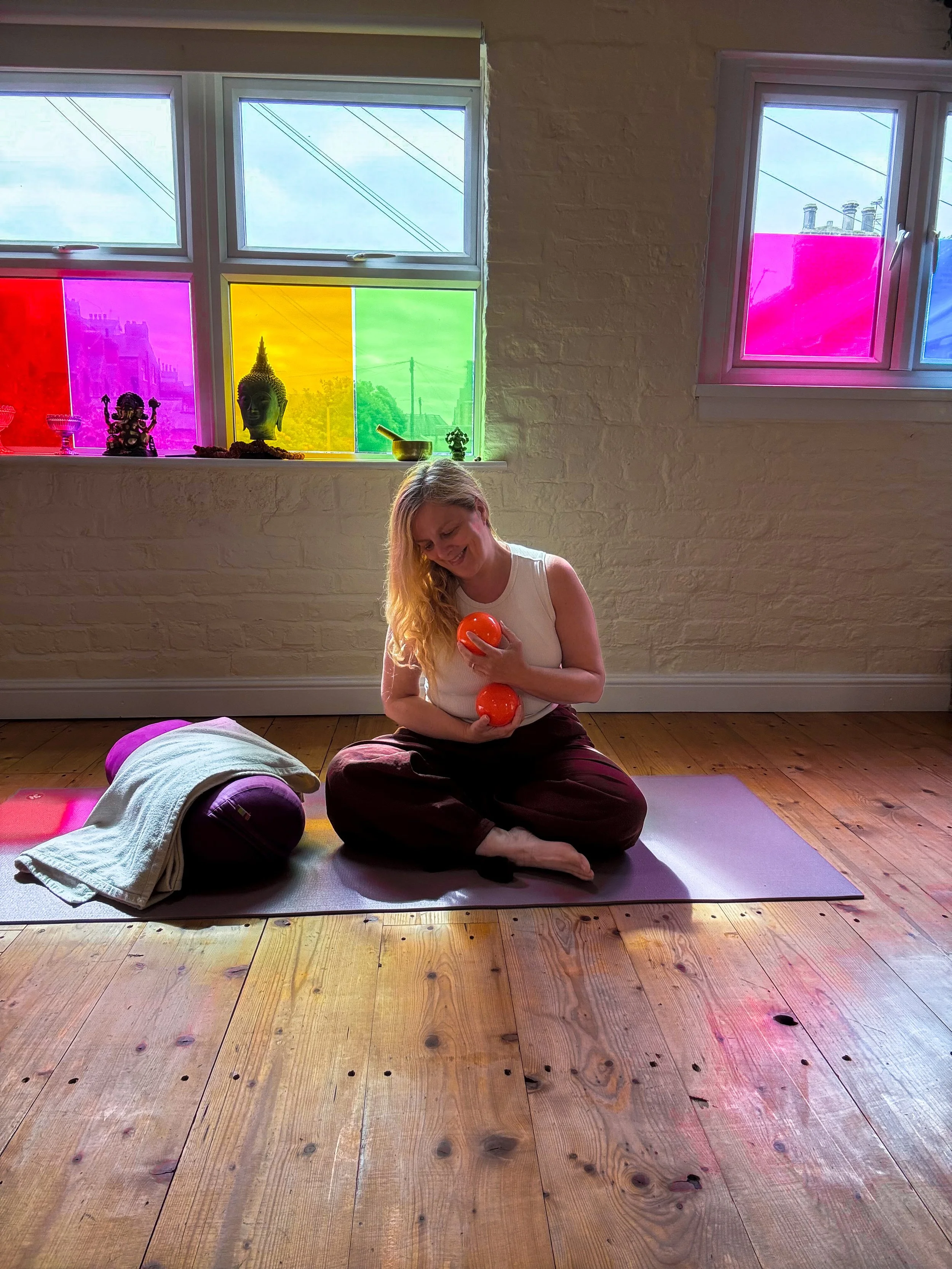 Sarah Pritchard MSMT MSME, Level 4 Franklin Method Educator, holding orange Franklin Method balls in the light-filled studio at The Stables Yoga Centre in York.