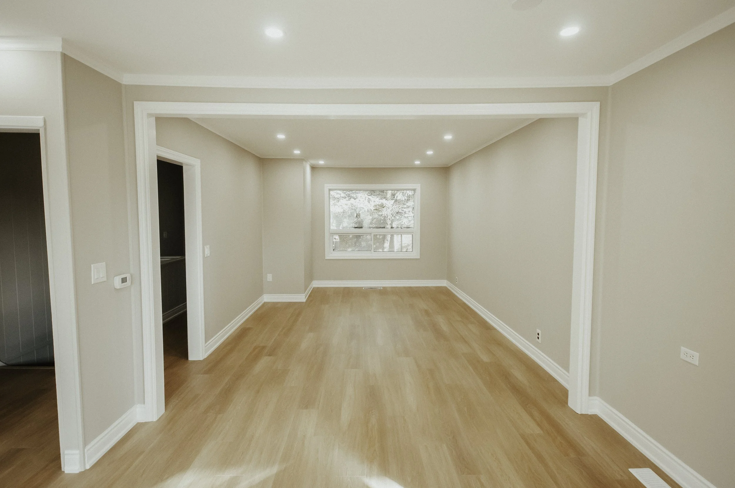 Empty room with beige walls, hardwood flooring, a window letting in natural light, and recessed ceiling lights.