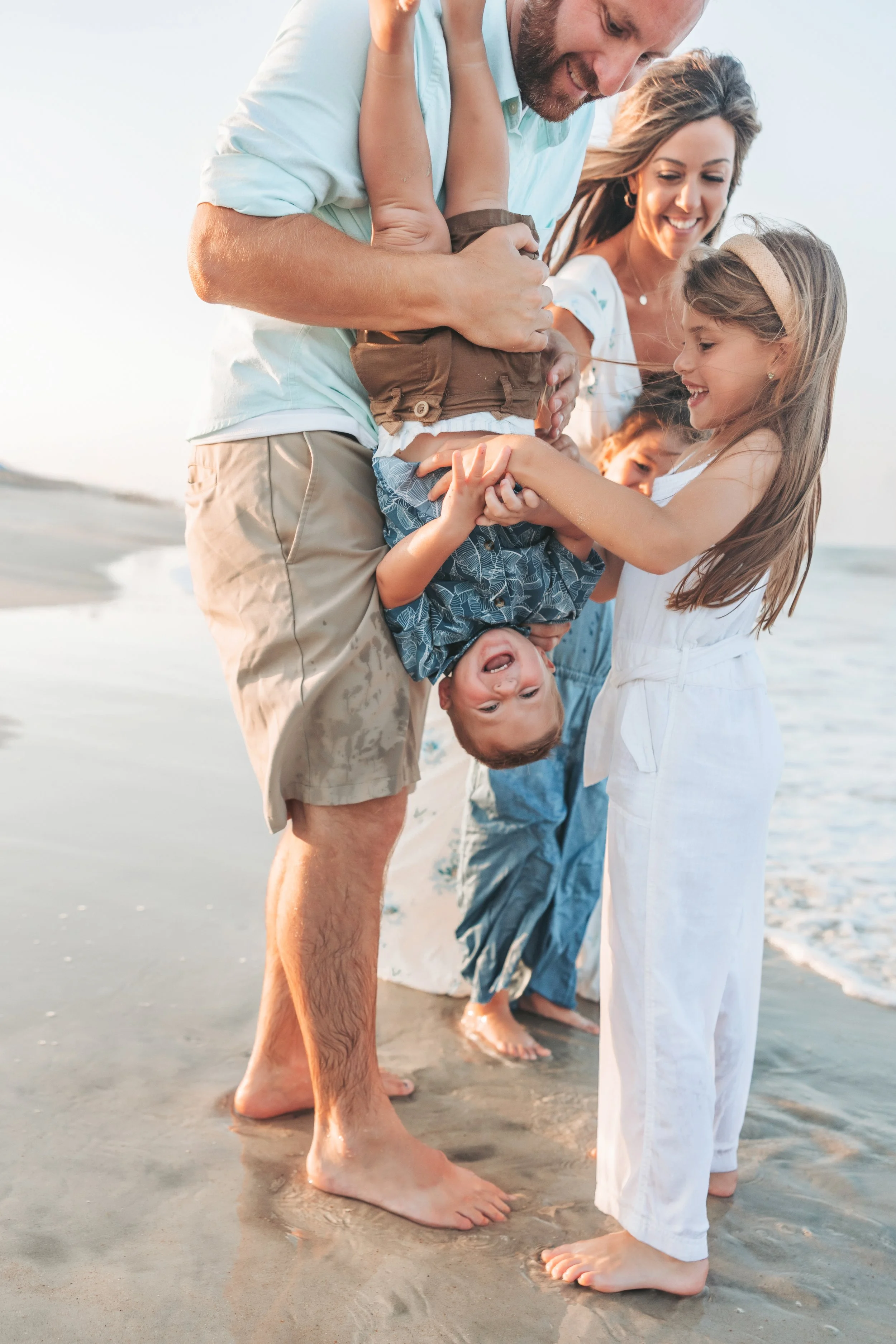 A happy family of children and adults on a beach, playing and laughing together during sunset.