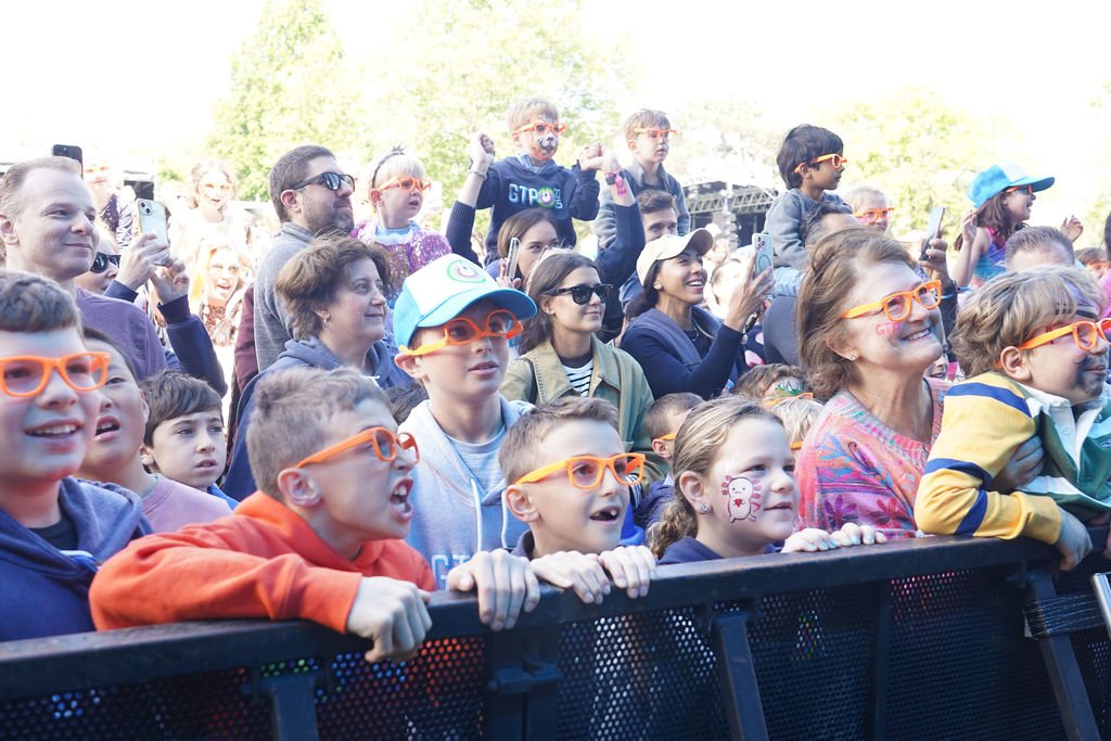 A crowd of children and adults wearing orange glasses and enjoying an outdoor event.