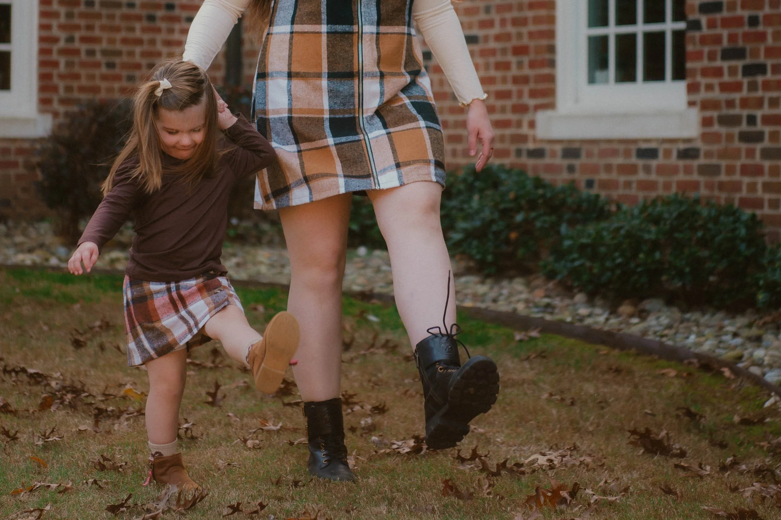 mother and daughter kicking their feet out while walking. Dressed in a fall plaid dress/skirt