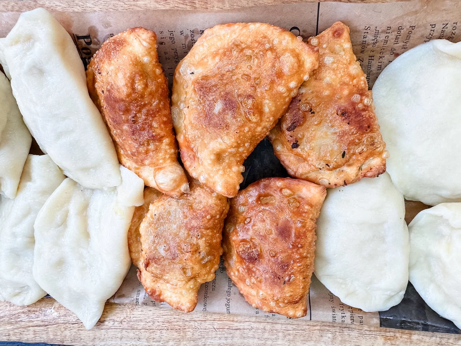 Traditional Polish pierogi served both boiled and pan-fried on a wooden tray in Poland.