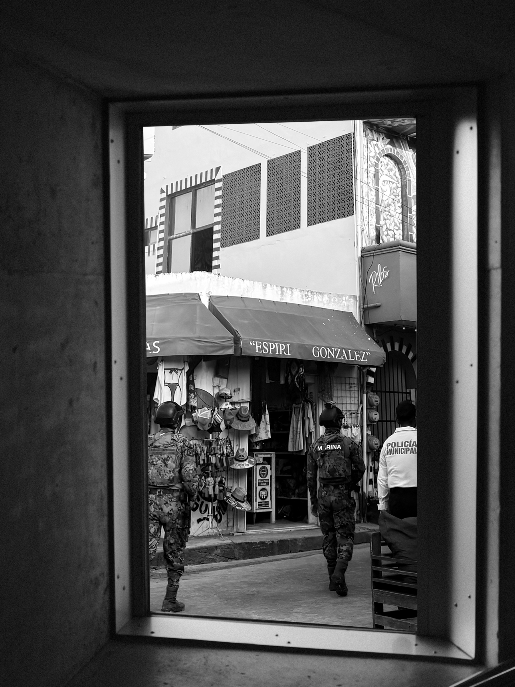 Seen through a window inside, la policia walking the streets in Las Mujeres, Mexico in black and white