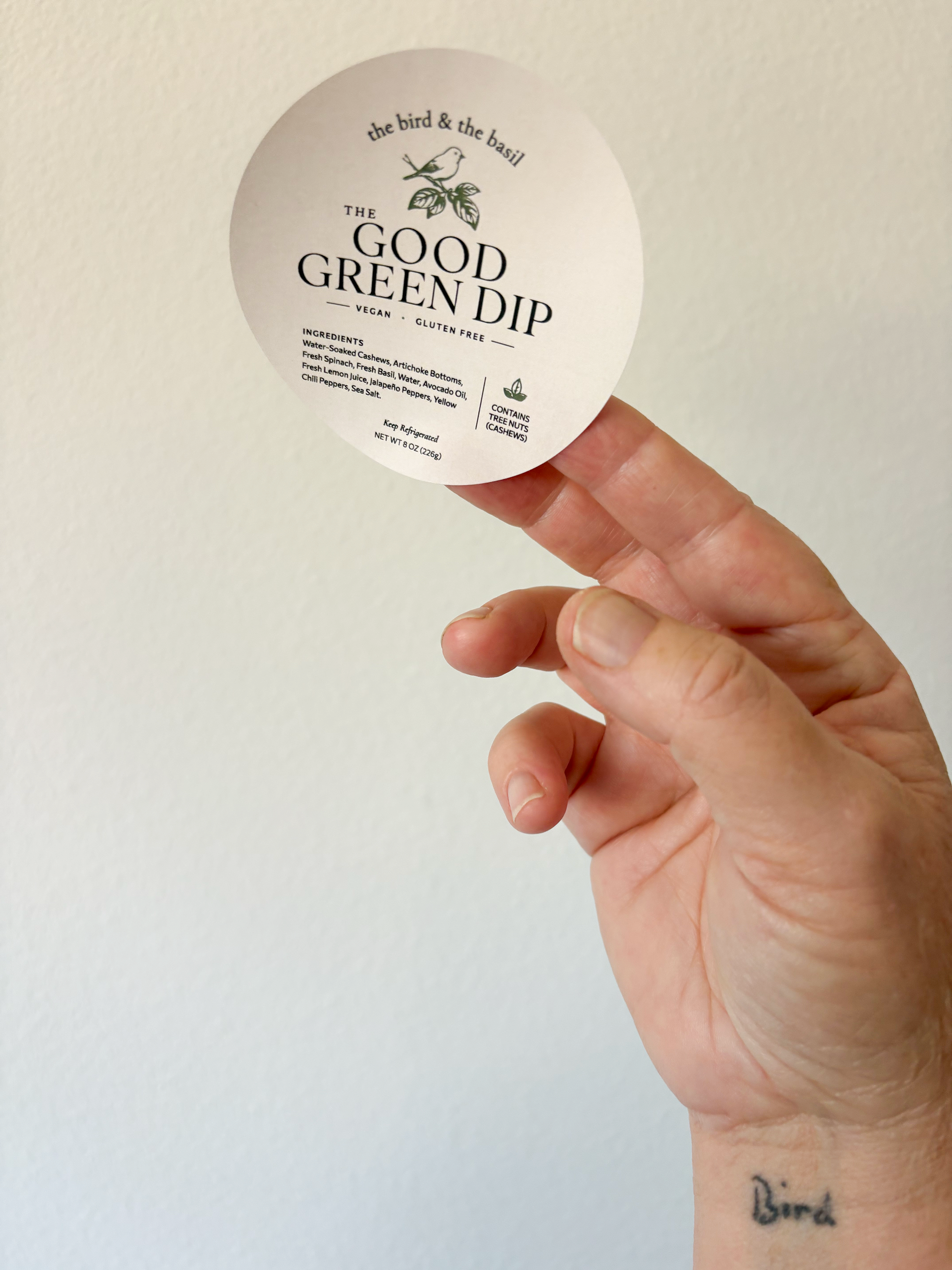 The bid & the basil The Good Green Dip label in hand against white wall