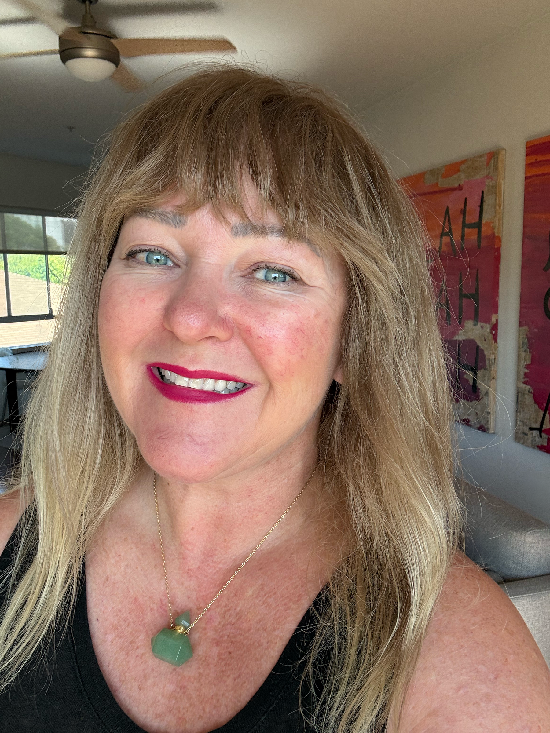 Julia Gomelsky smiling at camera at home in living room with artwork that has "Blah Blah Blah" painted on canvas in the background