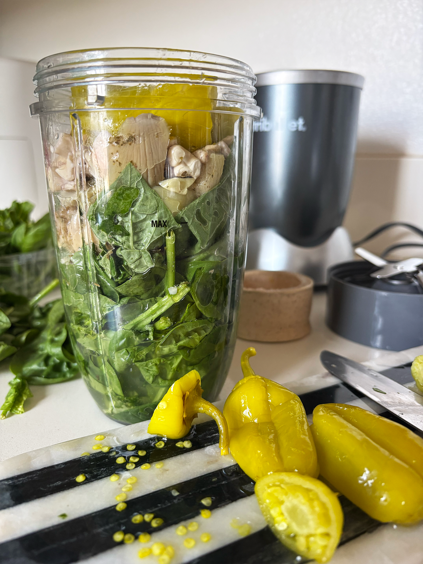 Pepperochinis in the foreground with spinach, basil and other ingredients in a nutribullet in the background