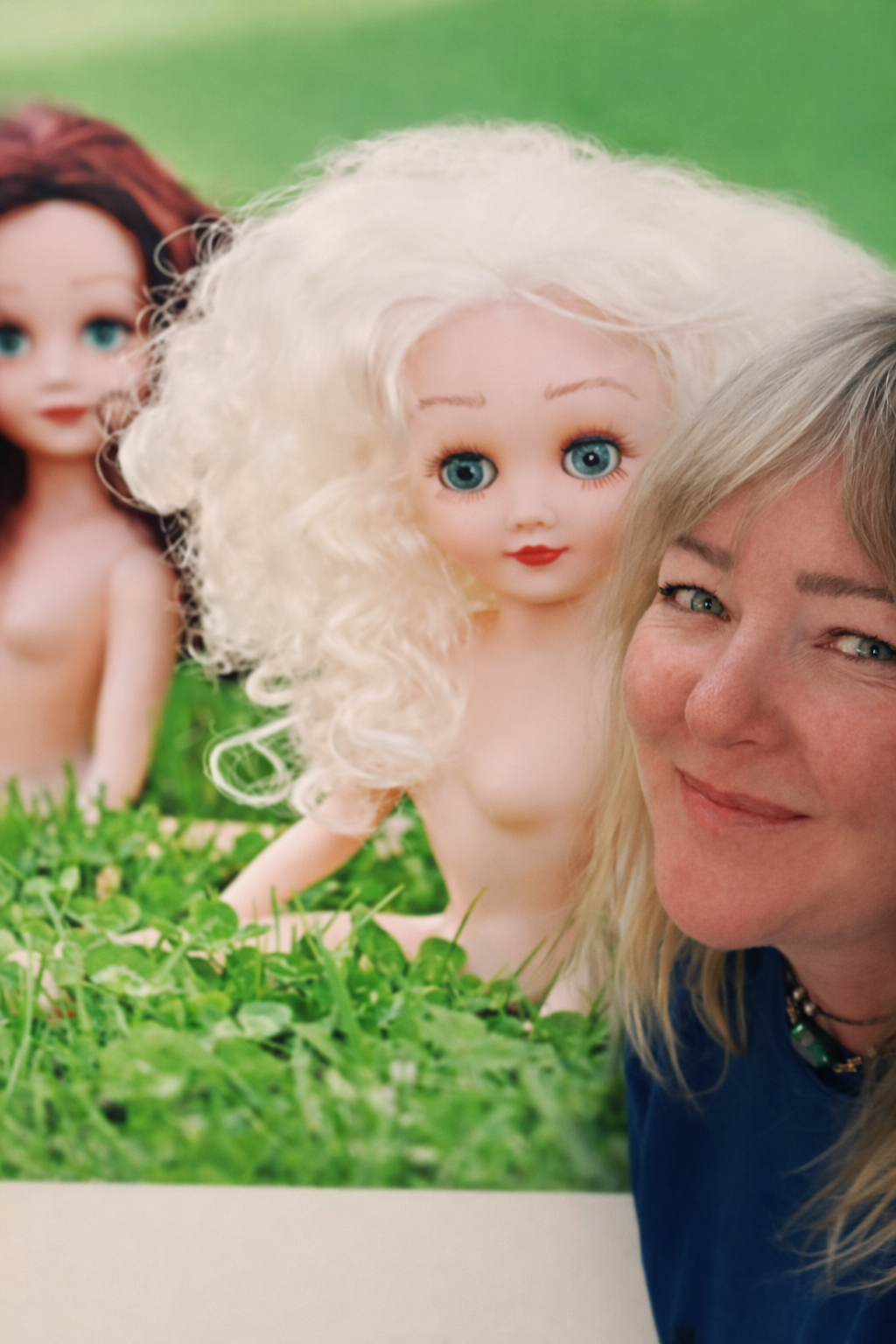 Julia Gomelsky smiling at camera with "Where the Grass is Greener" canvas with Paige and Ginger doing the splits in the background