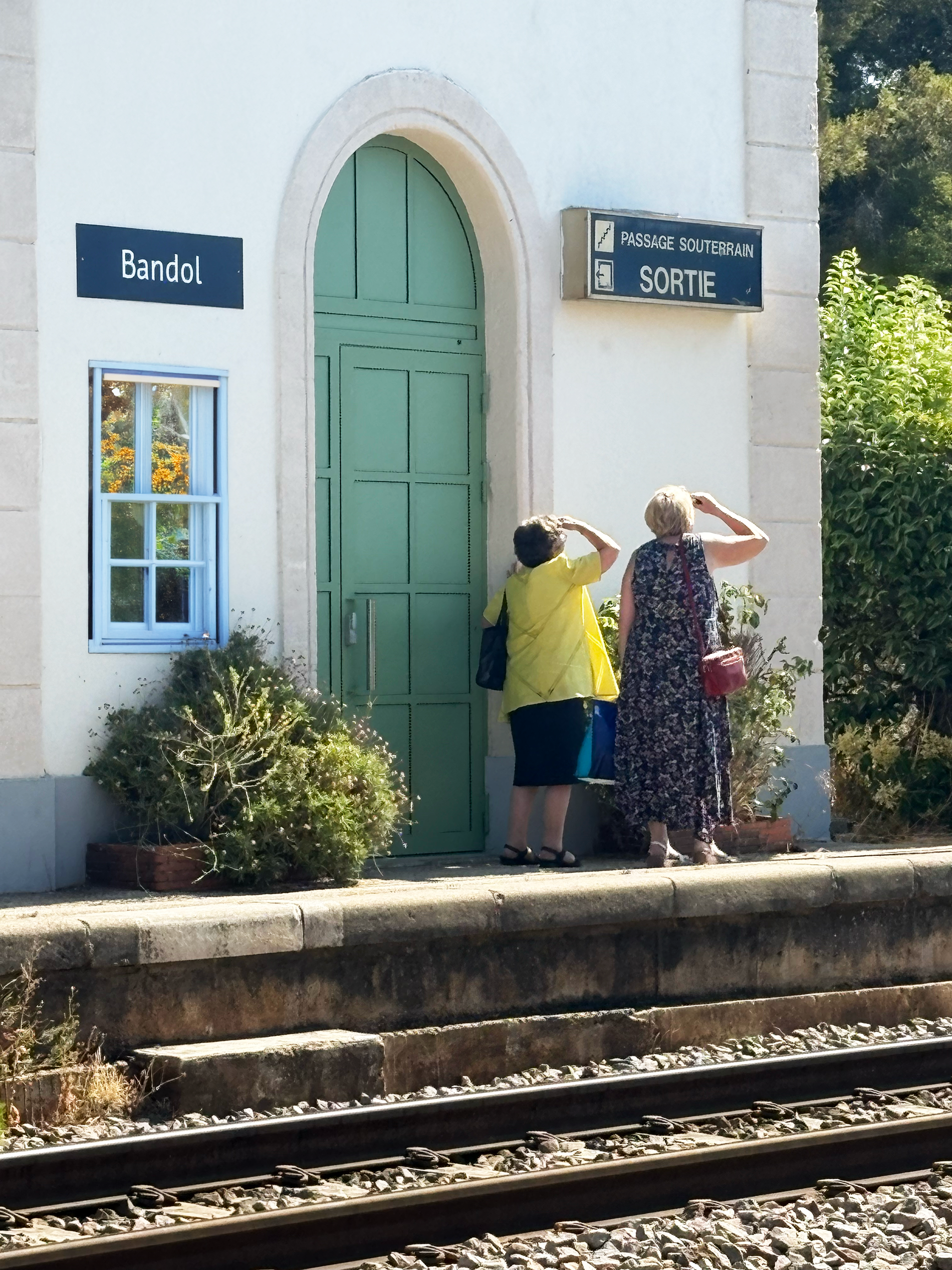 Bandol Biddies. Two old ladies with their arms up covering eyes from sun at the Bandol train station
