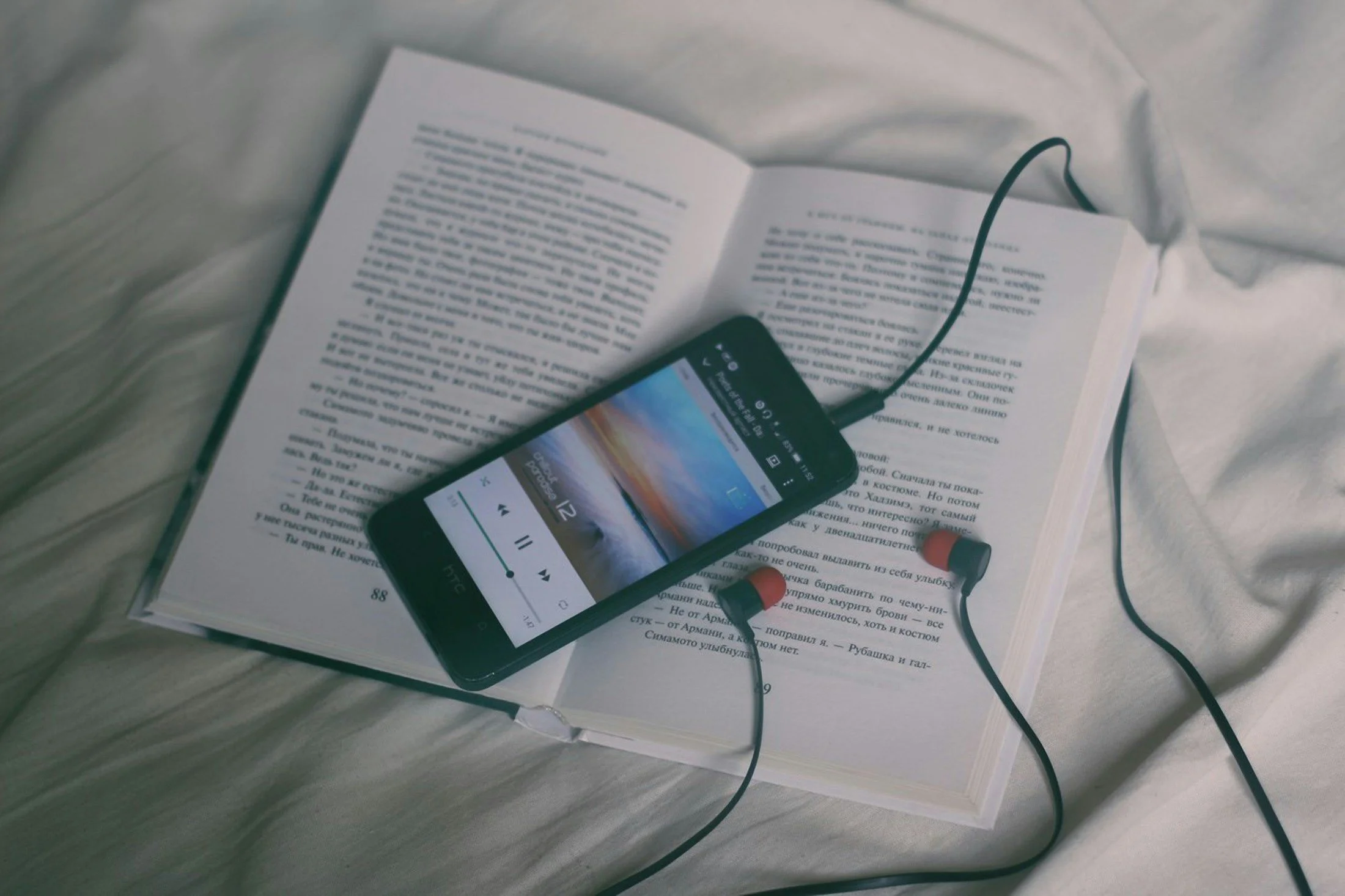 Audiobook playing on a cellphone with headphones plugged in laying on top of a book