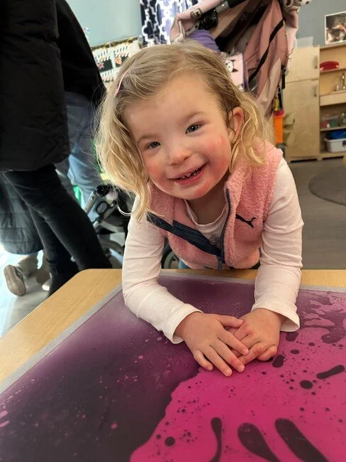 A little girl leaning on a sensory mat and smiling