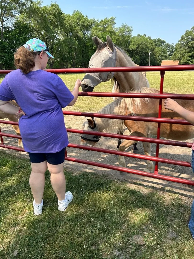 A People with Purpose participant standing in front of a red gate where two horses are standing