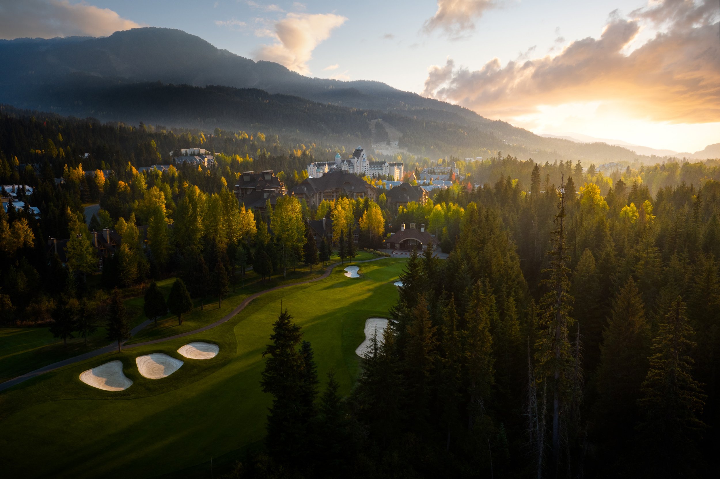 sunset over Whistler mountain landscape with Fairmont Chateau Whistler golf course in the foreground, surrounded by dense trees.